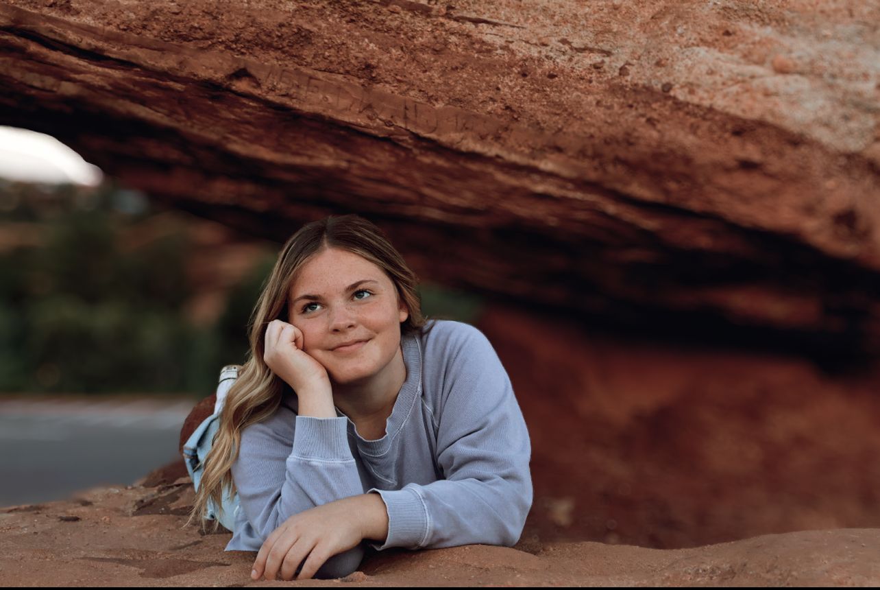 Young woman posing under red rock formation at Garden of the Gods, Colorado Springs senior portrait photography.
