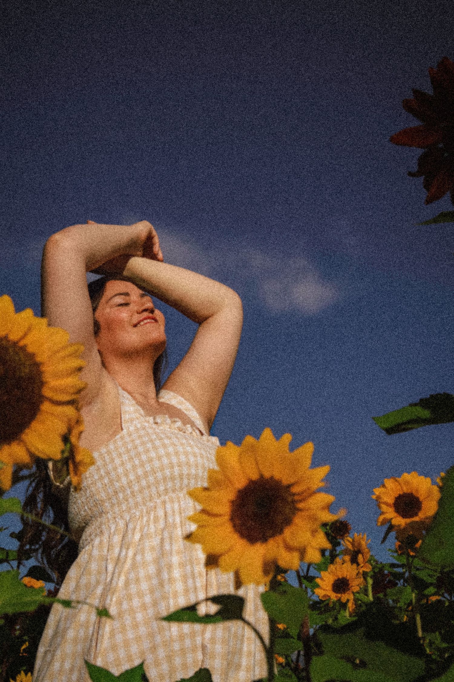 Creative outdoor portrait of a young woman posing among tall sunflowers under a blue Colorado sky.