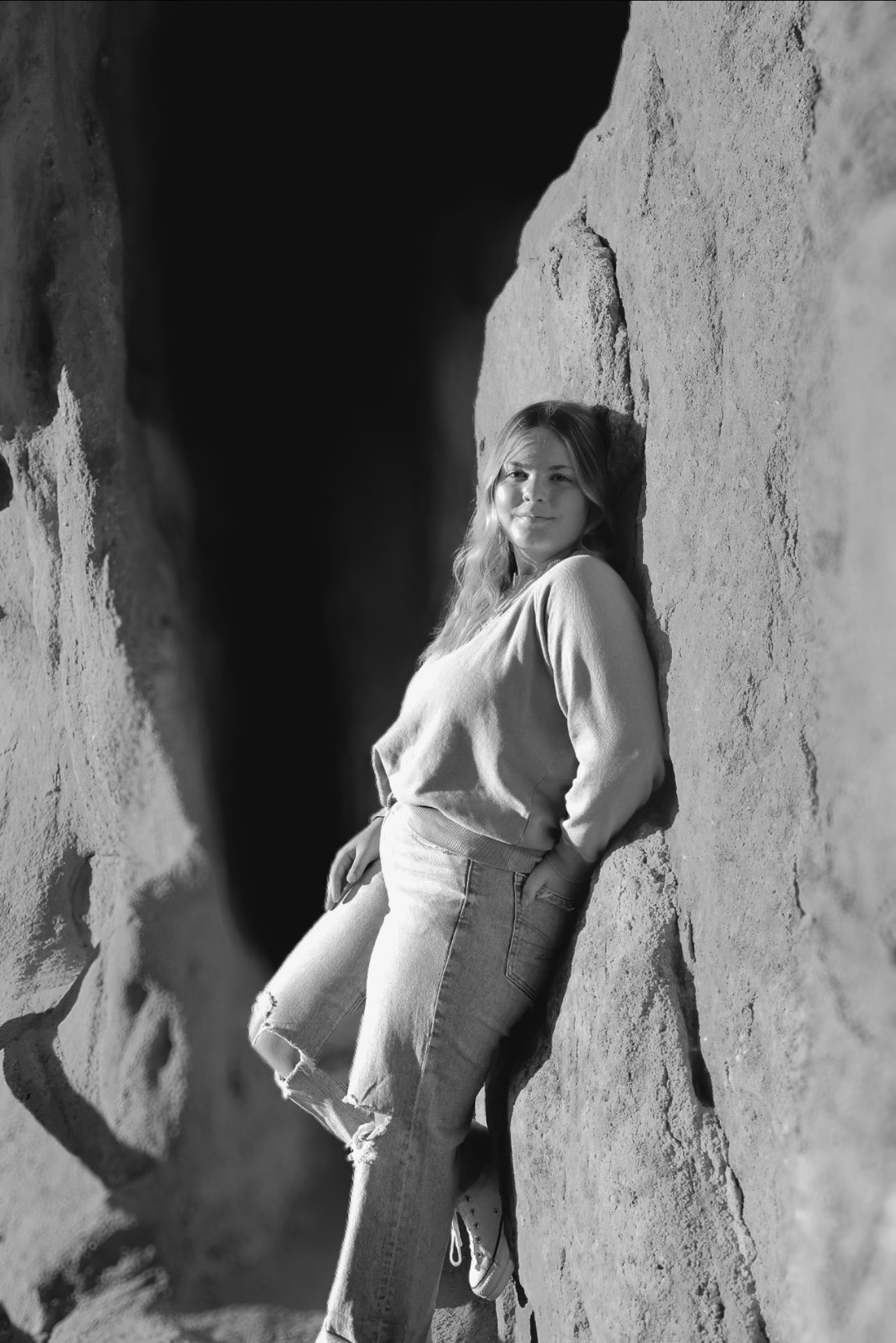 Black and white portrait of a female high school senior leaning against a red rock formation during a senior photography session.