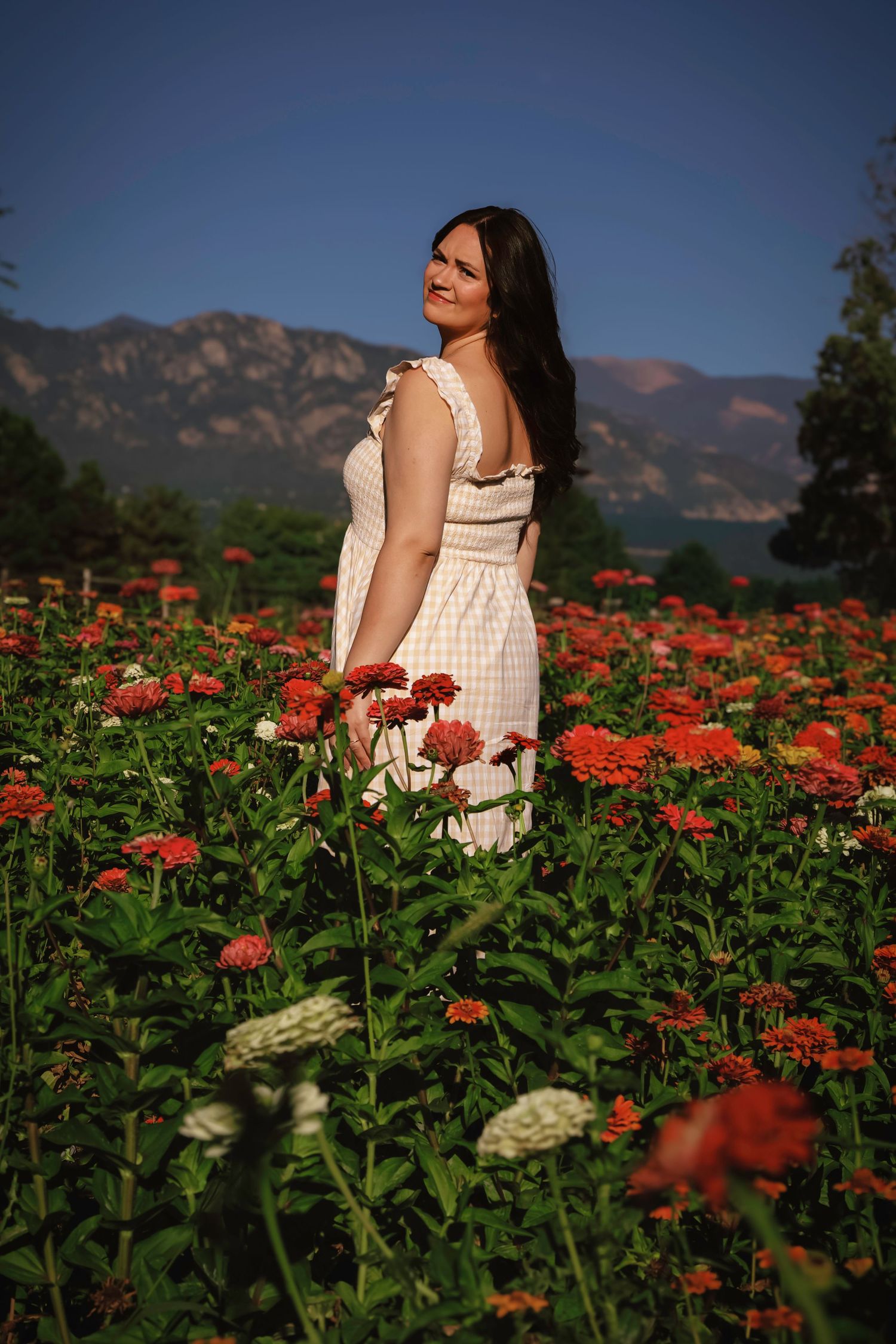 Young woman standing in a flower field with Colorado mountain views during an outdoor portrait session.