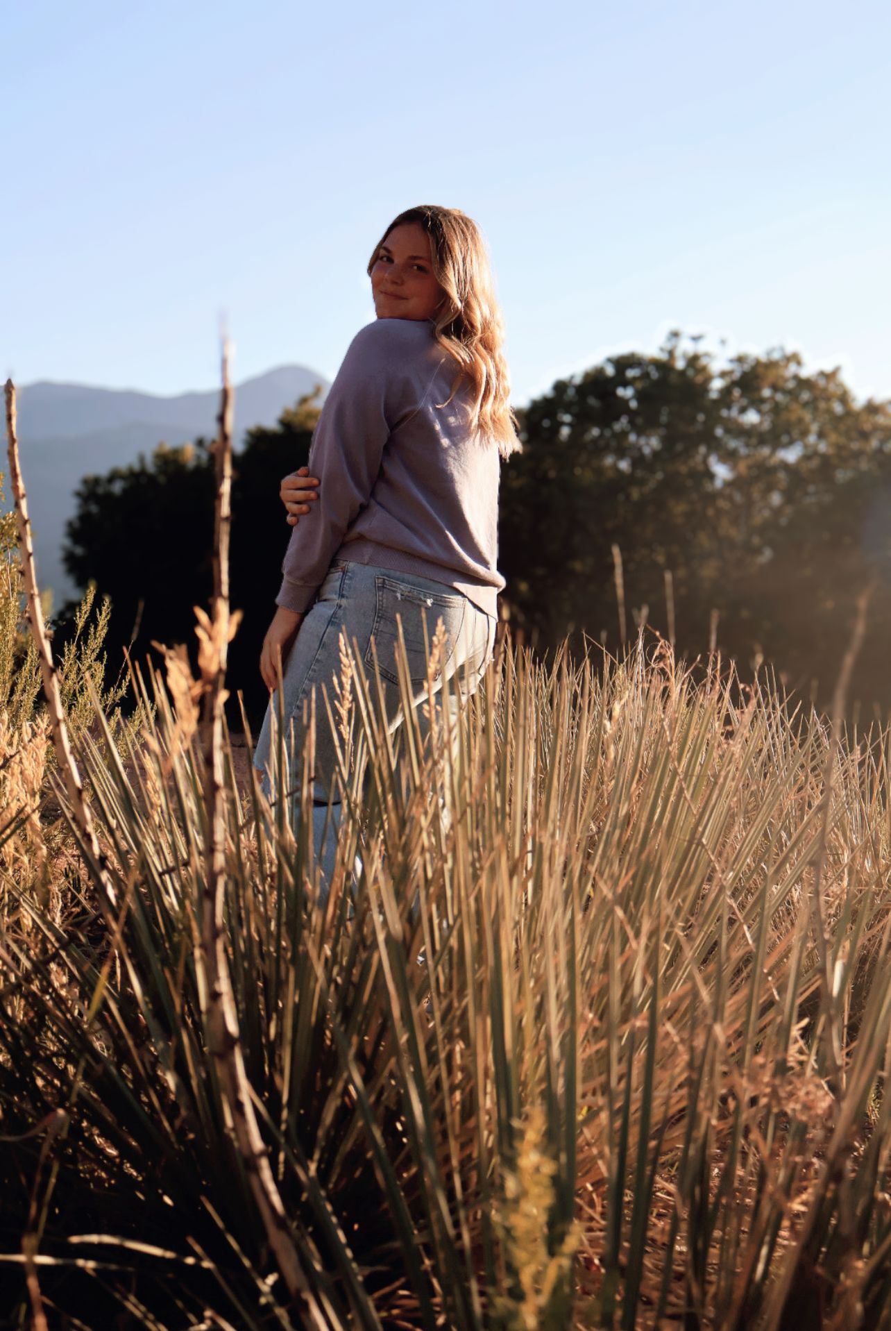 female high school senior standing in grassy field with Colorado mountain views during a Garden of the Gods senior photography session.