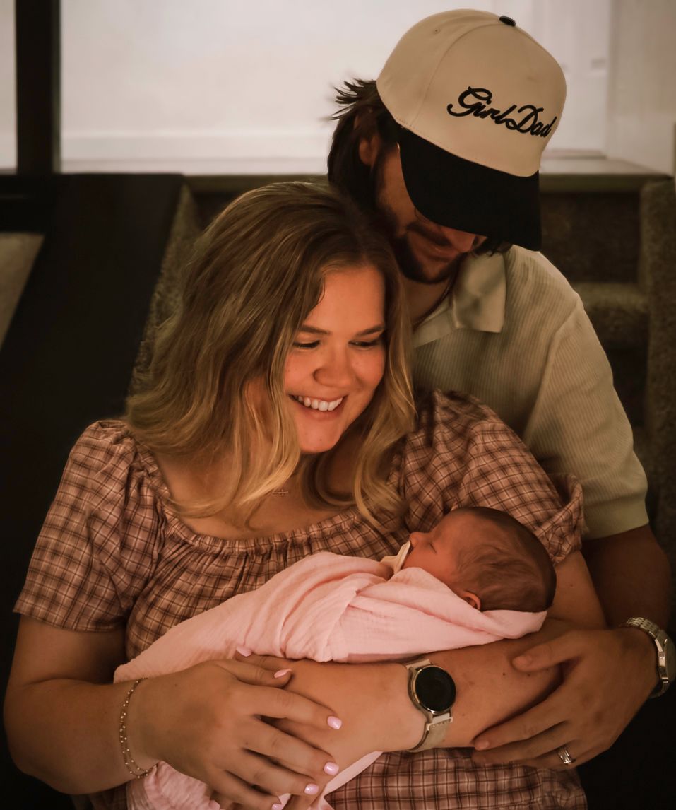 New parents smiling together while holding their newborn baby during a lifestyle in-home newborn photography session in Colorado Springs