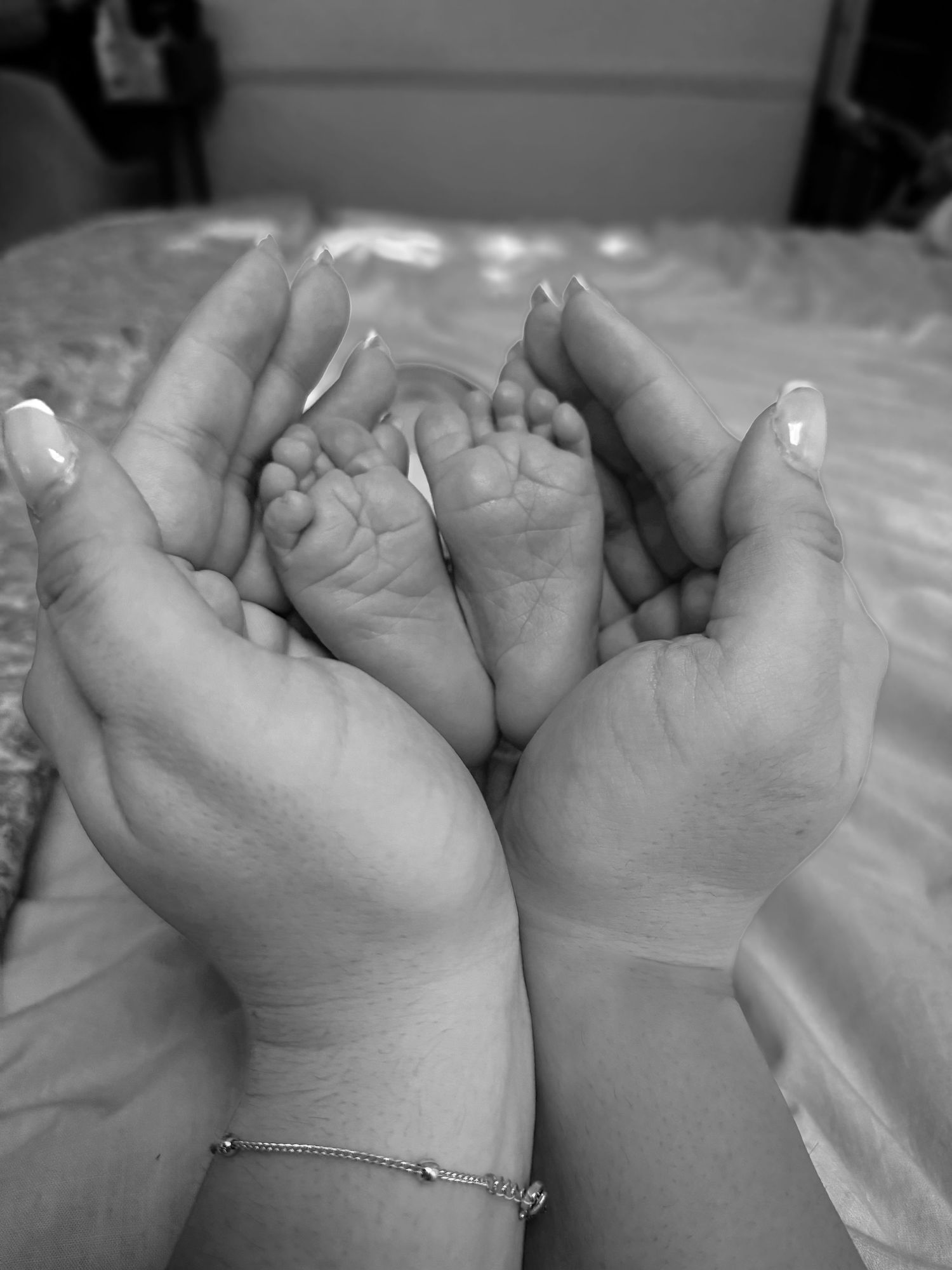 Black and white close-up of a newborn baby's tiny feet held gently in a parent's hands.