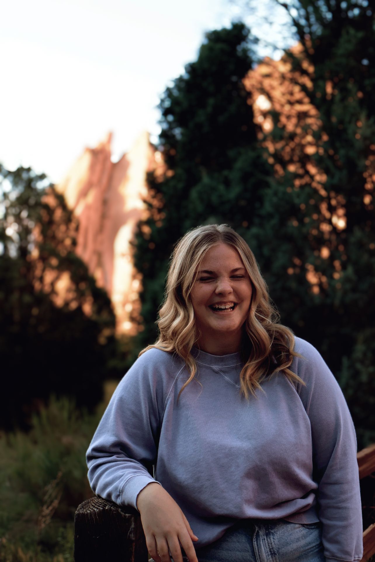 Smiling female high school senior posing with iconic red rock formations during a senior portrait session at Garden of the Gods.