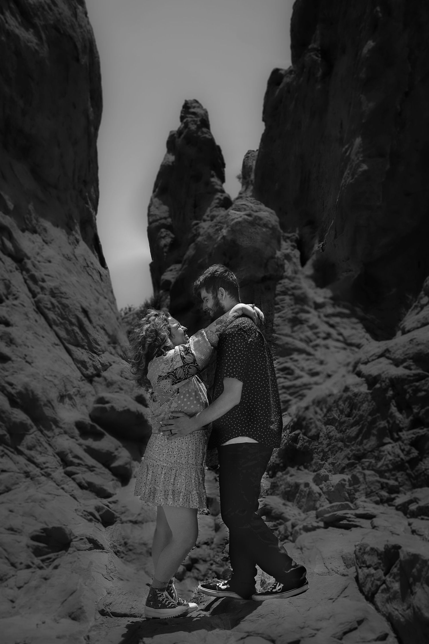 Black and white photo of a romantic couple embracing between dramatic rock formations in a canyon.