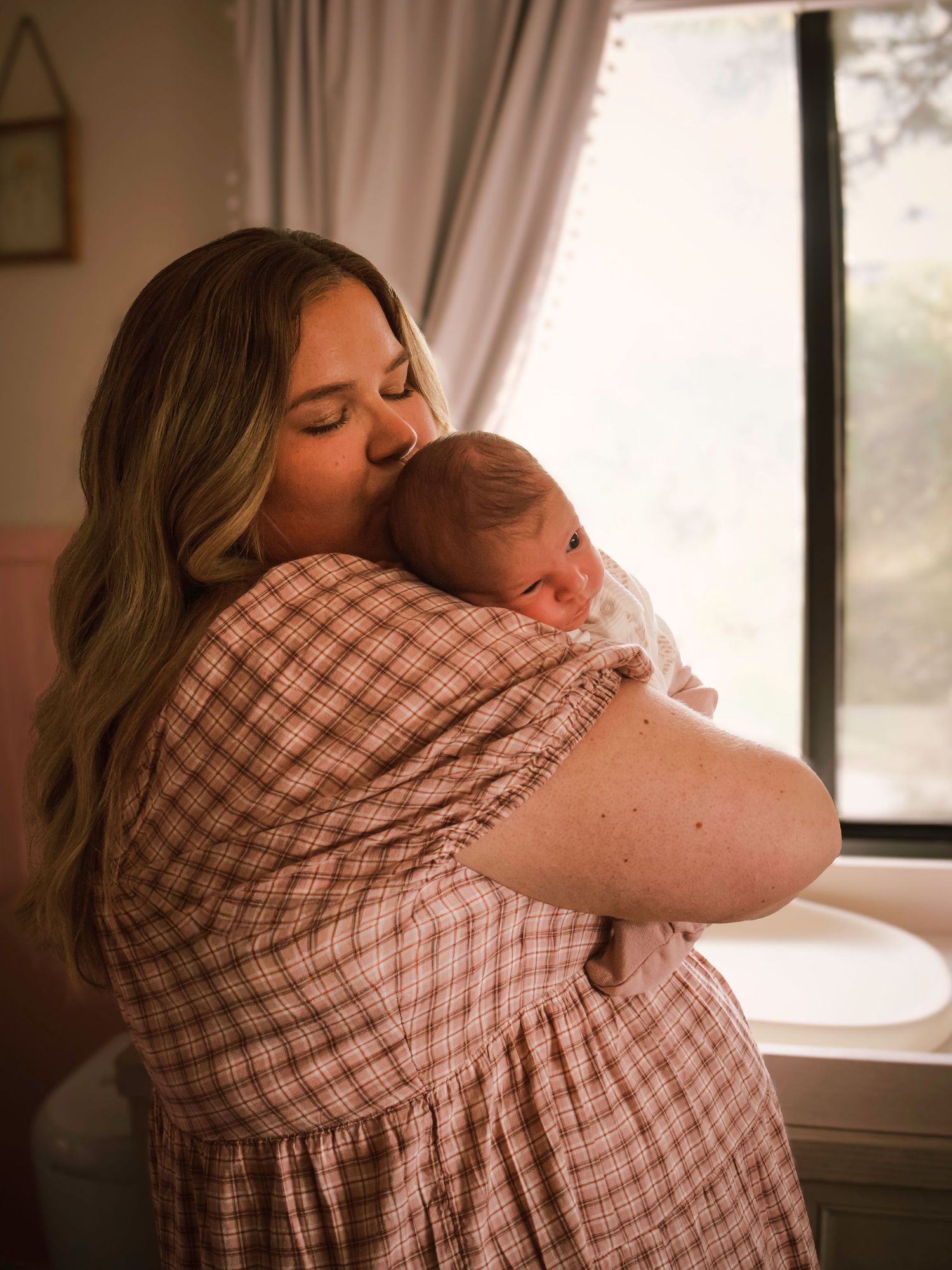 Mother cuddling her newborn baby near a window during a natural in-home newborn photography session in Colorado Springs, Colorado