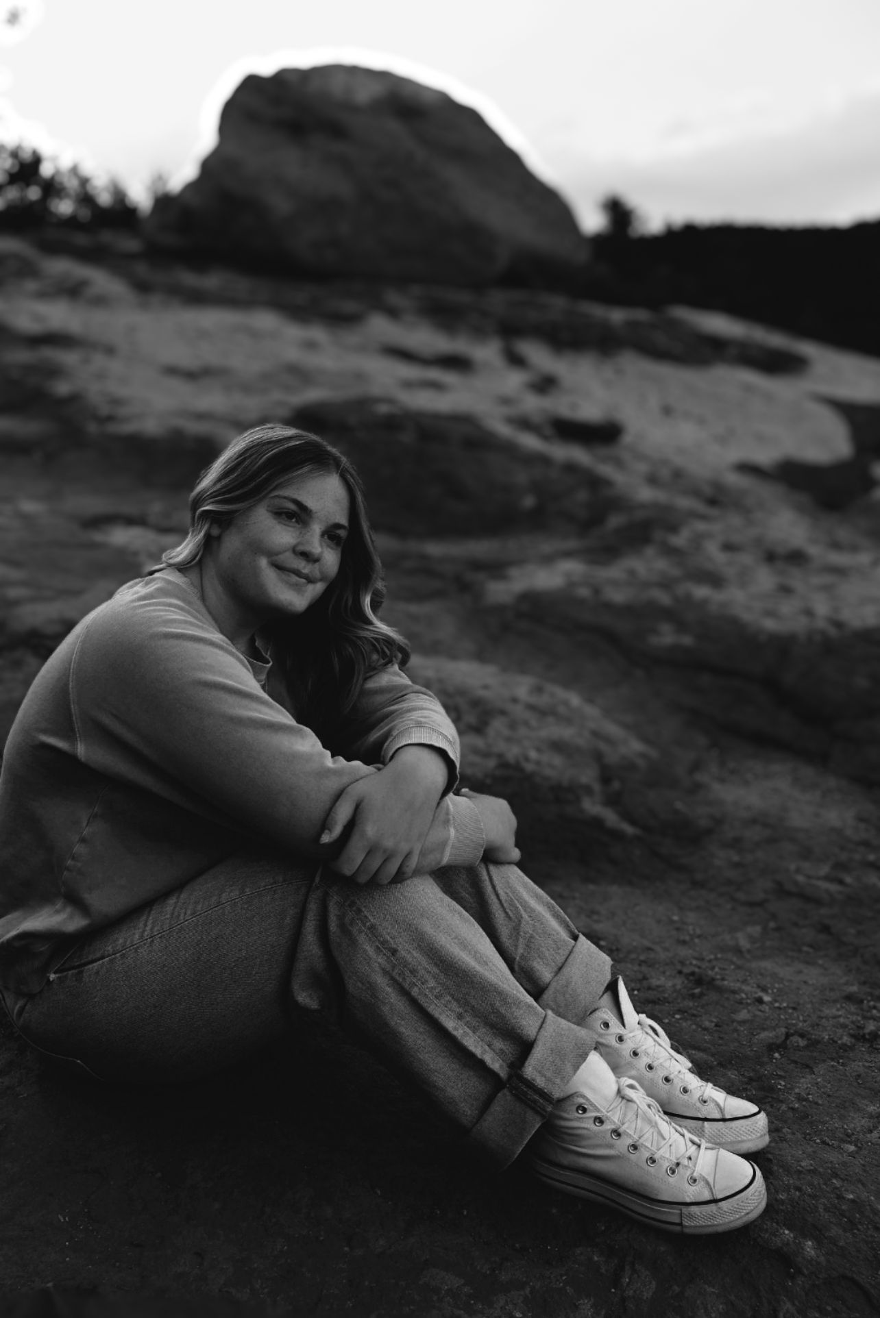 Black and white senior portrait of a female high school senior siting on red rocks at Garden of the Gods in Colorado Springs, Colorado.