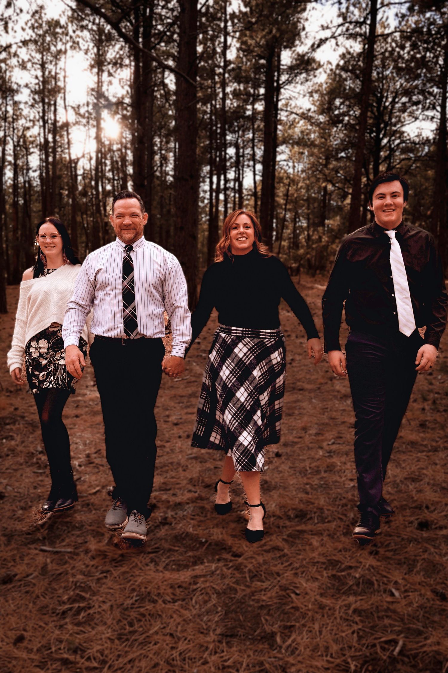 Family of four walking through the pine trees during an outdoor family photography session at Fox Run Regional Park in Colorado Springs, CO.
