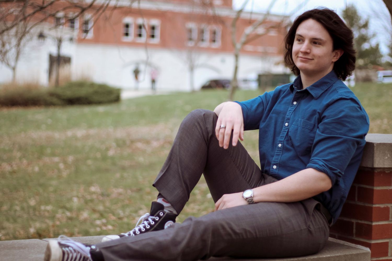 A person sitting casually on a brick ledge outdoors, wearing a blue shirt and sneakers.