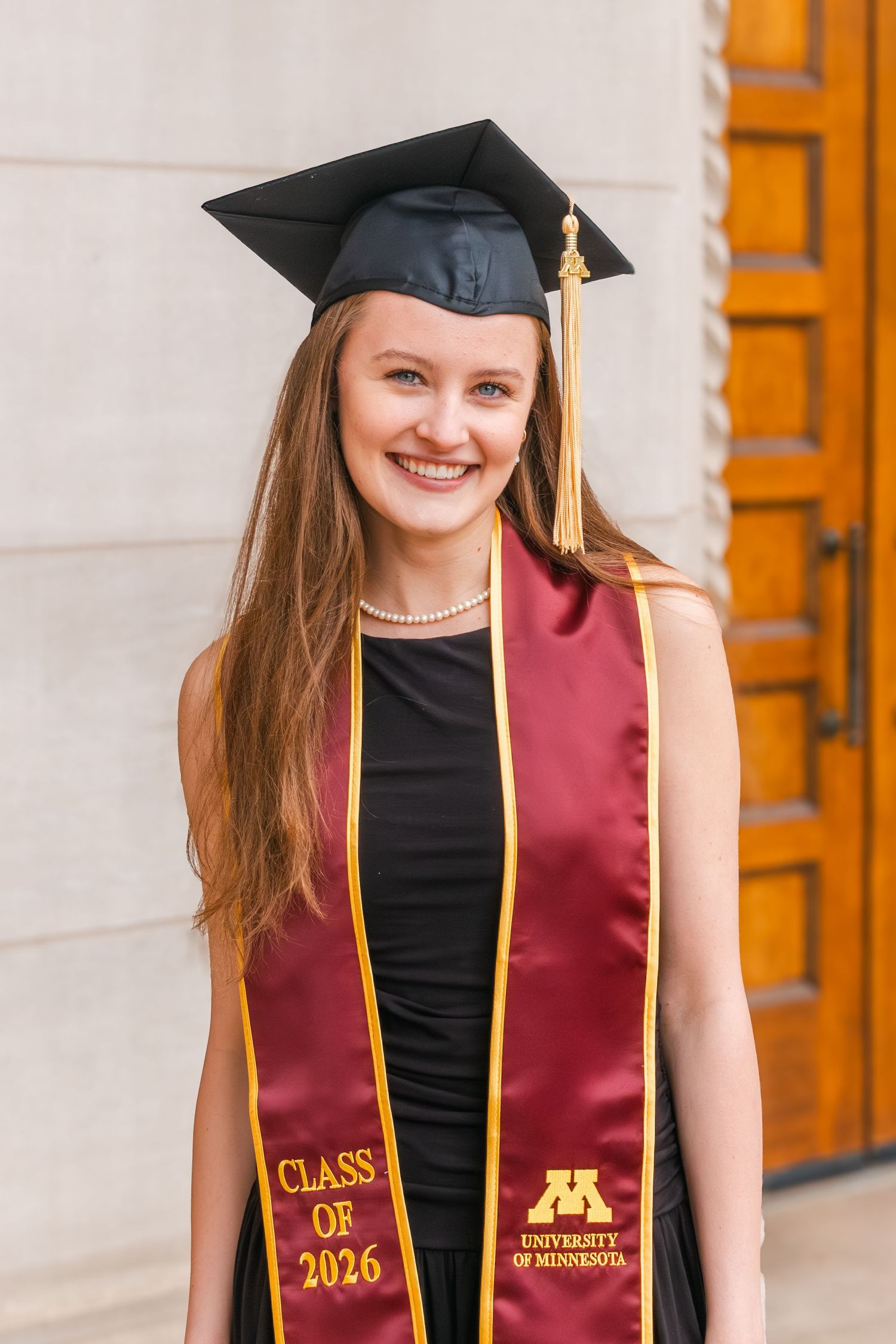 Smiling female graduate wearing black cap and maroon University of Minnesota Class of 2026 stole outdoors.