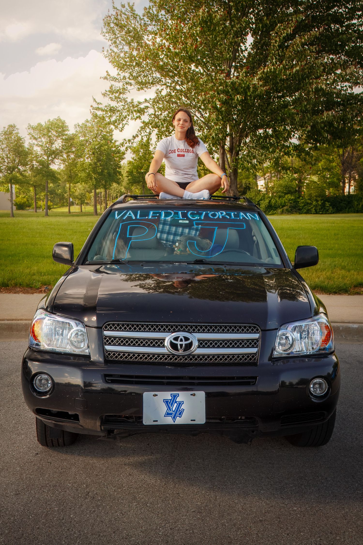 A Toyota SUV parked in a park setting with someone sitting in lotus position on the hood at sunset.