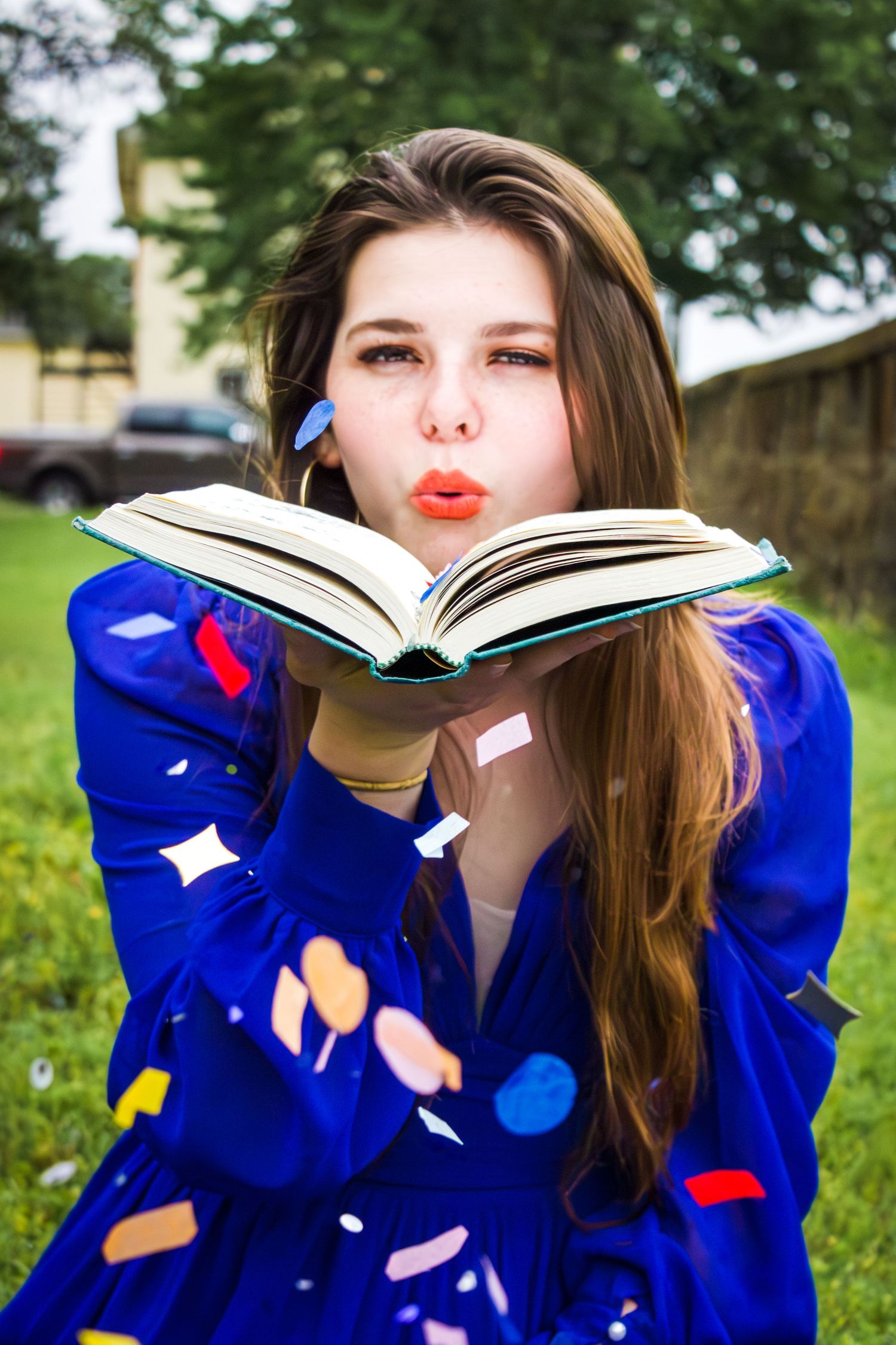 Person in blue dress blowing petals from an open book outdoors.