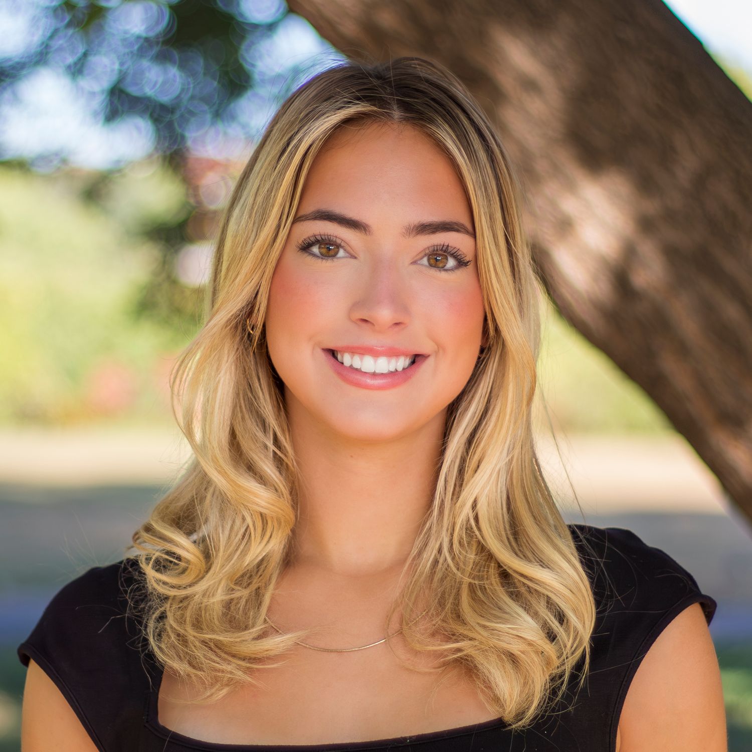 Outdoor portrait with blonde wavy hair, sunlit natural lighting creating a warm glowing effect in casual setting.