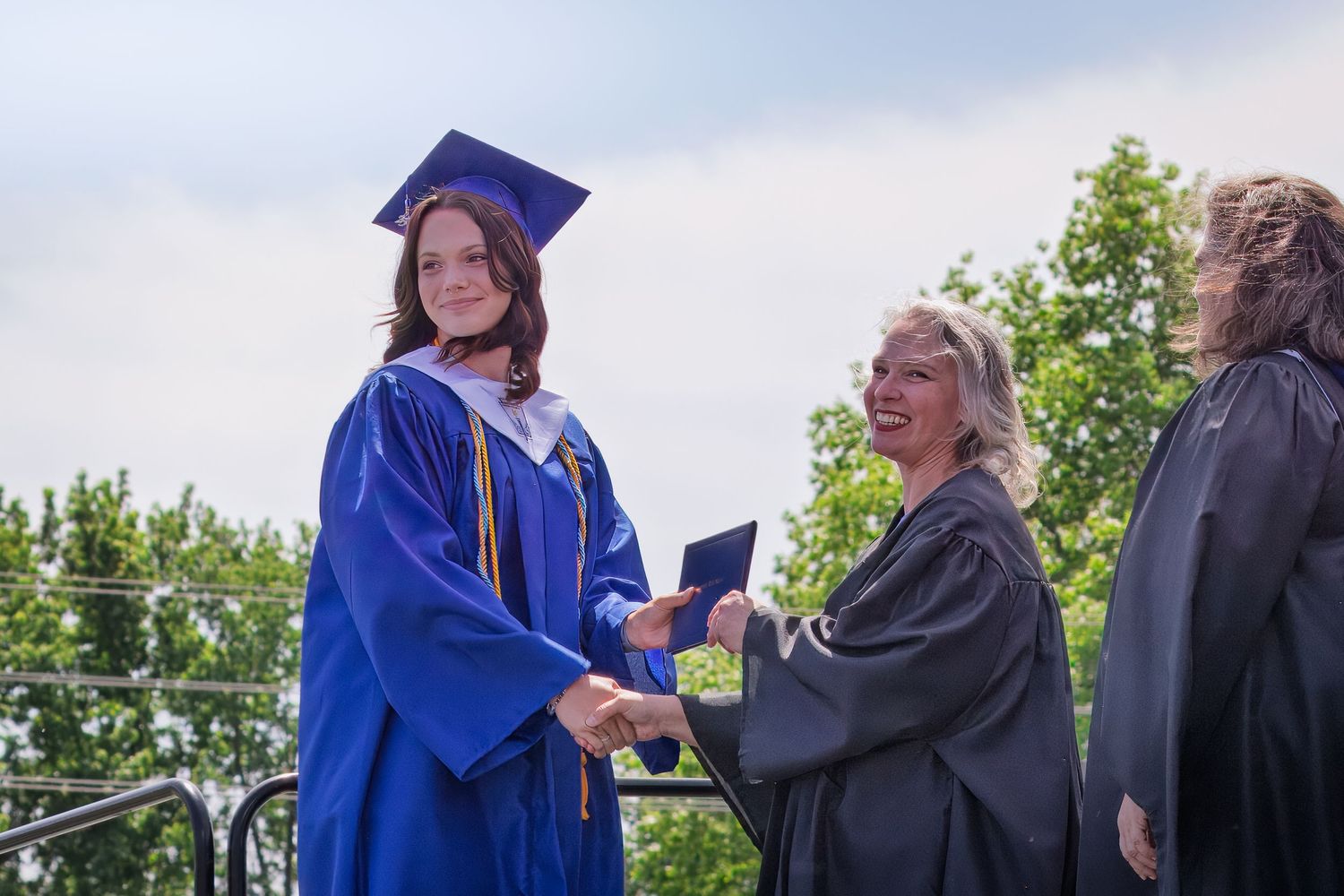 Graduate student in royal blue regalia shaking hands with faculty member during graduation ceremony.