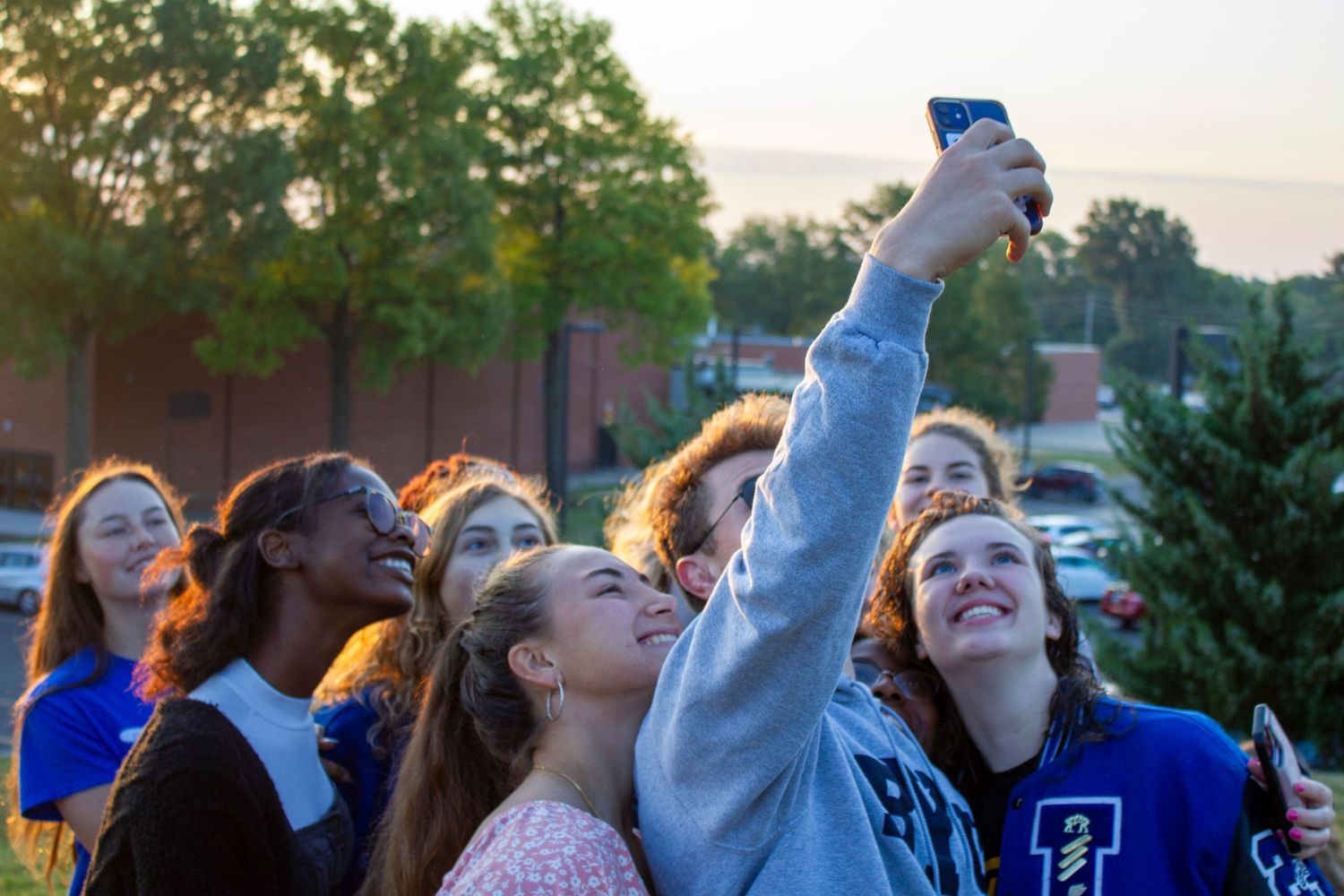 A group of enthusiastic students in blue school spirit wear celebrate together during an outdoor event.