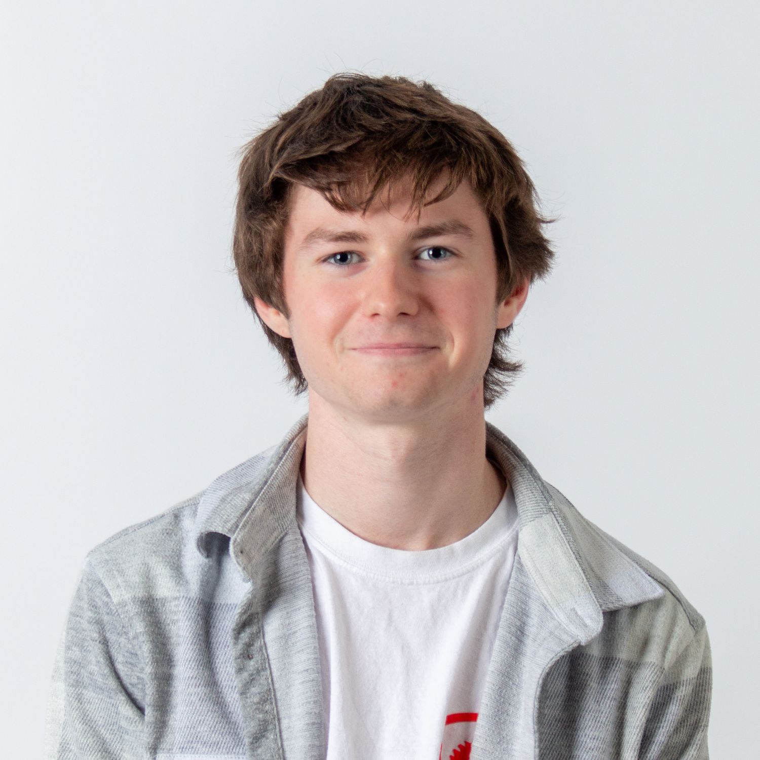 Young student in light gray jacket and white t-shirt poses with slight smile against white backdrop.
