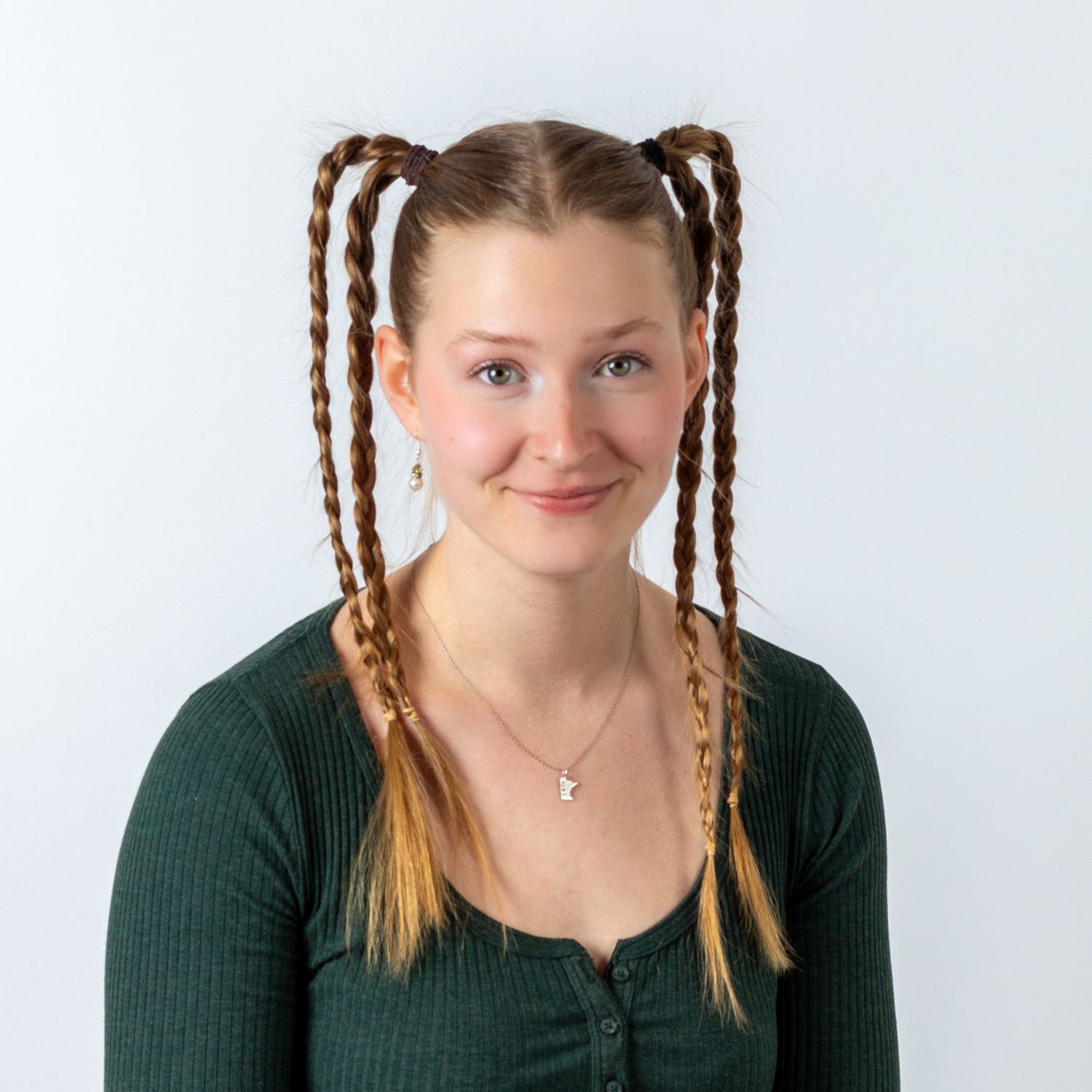 Studio portrait of someone with braided pigtails wearing a dark green ribbed sweater against a white background.