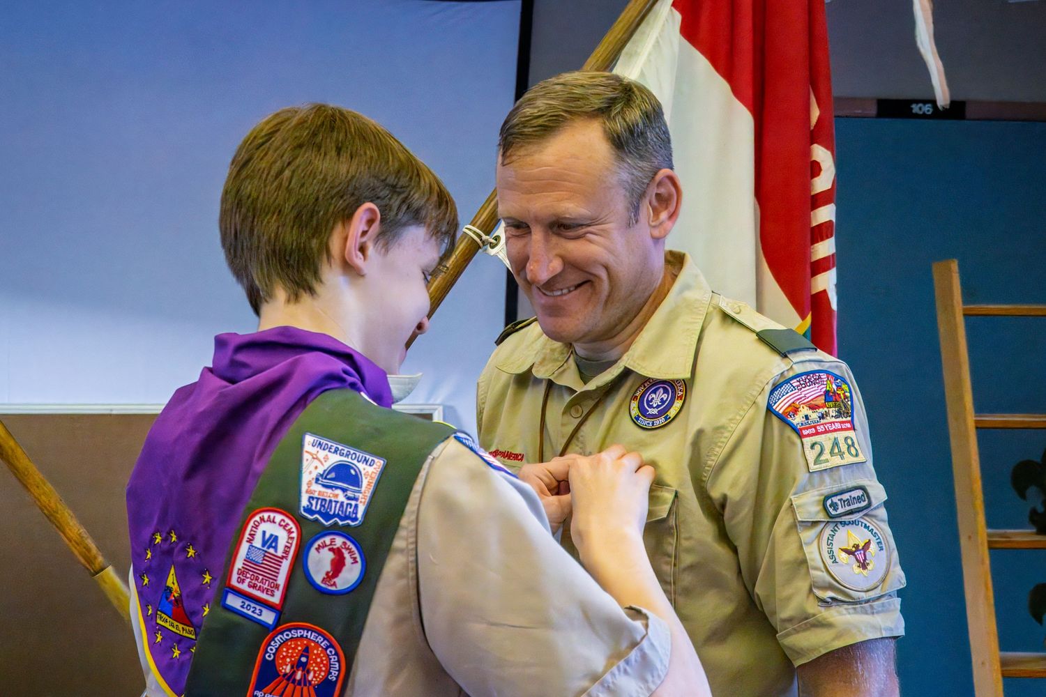 Two Scout members interact during a badge ceremony while wearing their uniforms with patches and insignias.