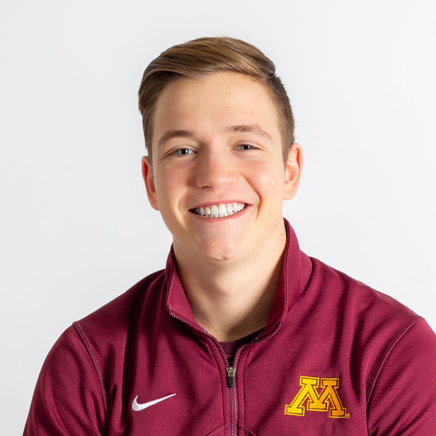 Athletic student wearing maroon University of Minnesota Nike quarter-zip jacket smiles against white background.