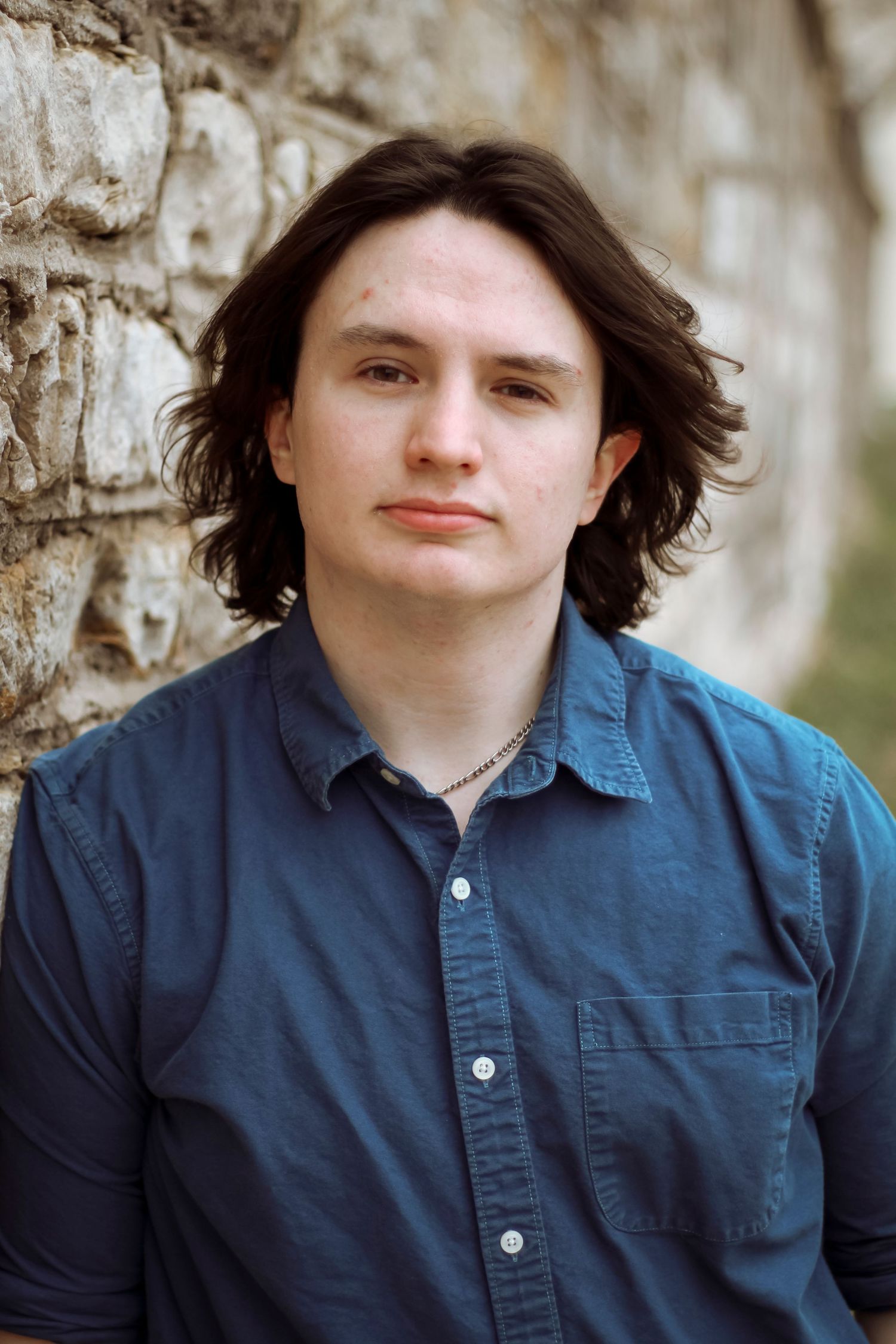 A set of four portrait photographs showing someone in a dark blue collared shirt against a stone wall background.