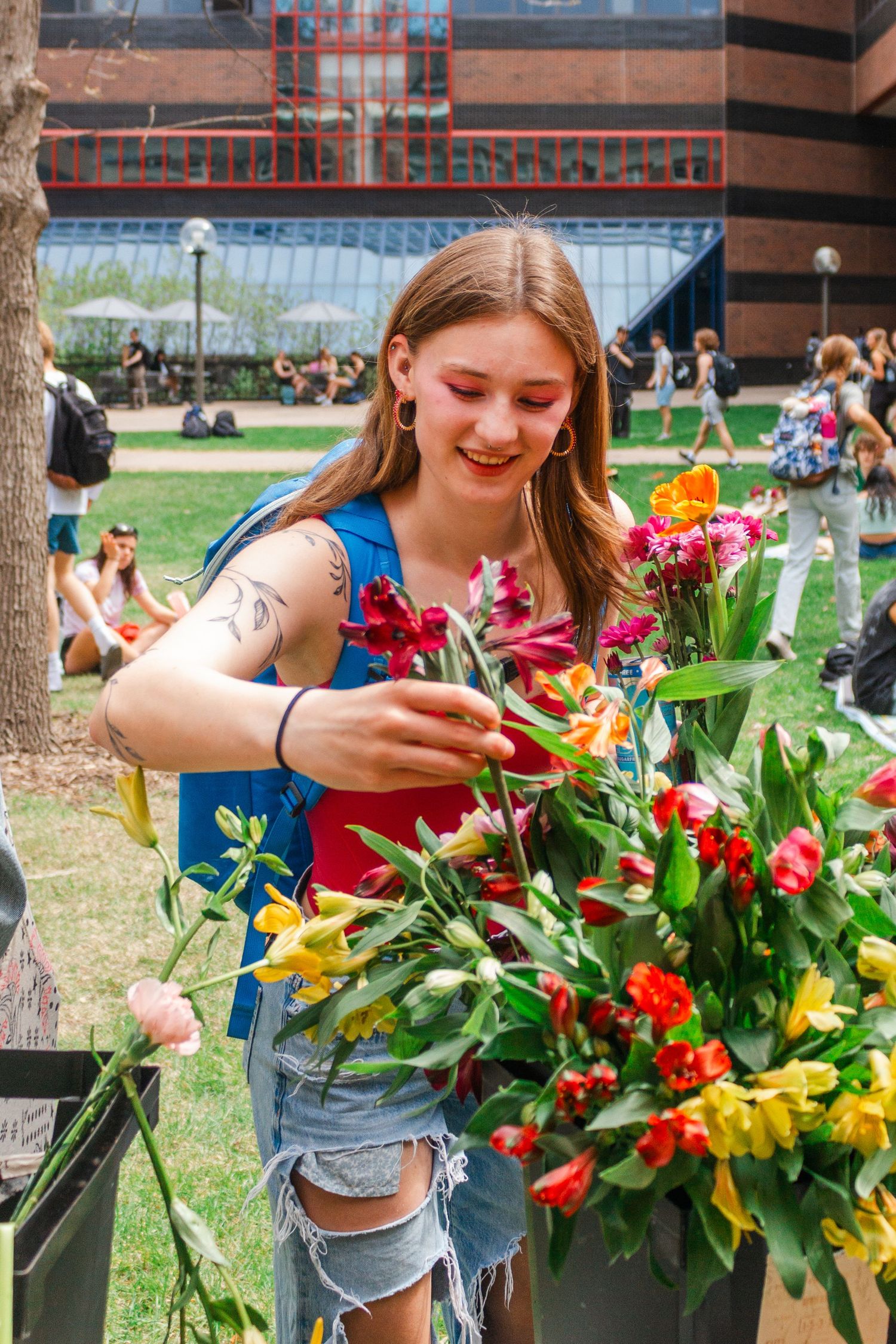 Young woman with face paint arranging colorful spring flowers outdoors at a sunny community event.
