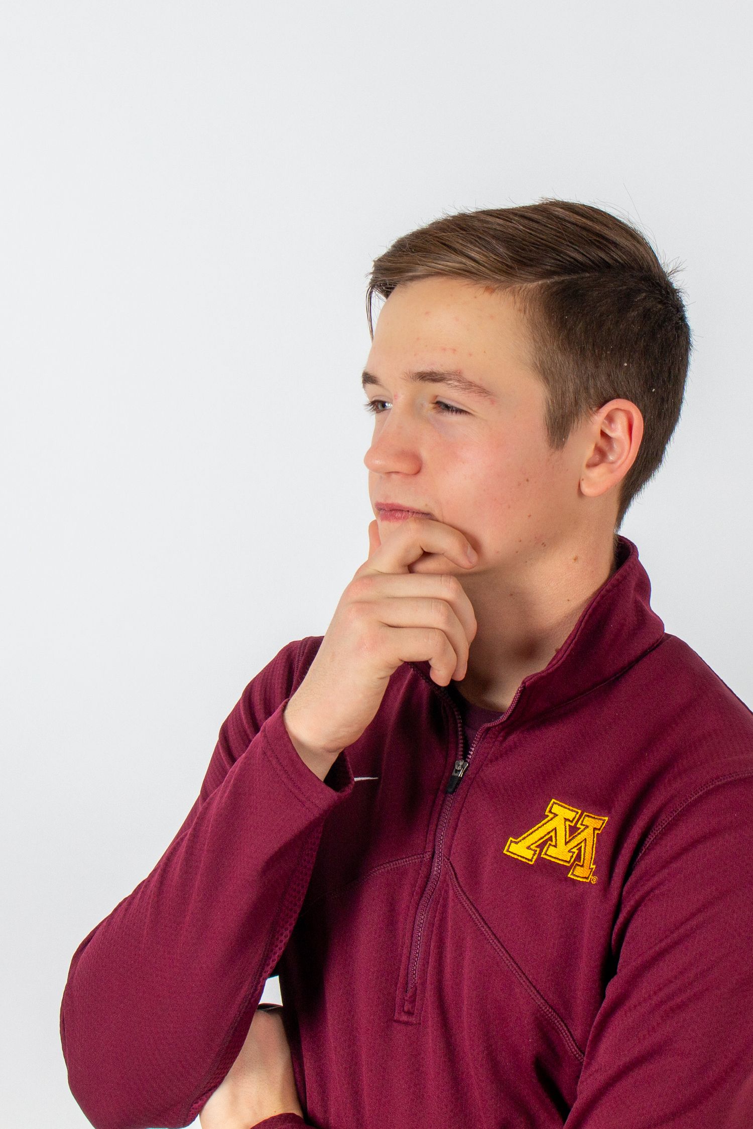 Person in maroon sweatshirt covering mouth with hand while looking to the side against white background.