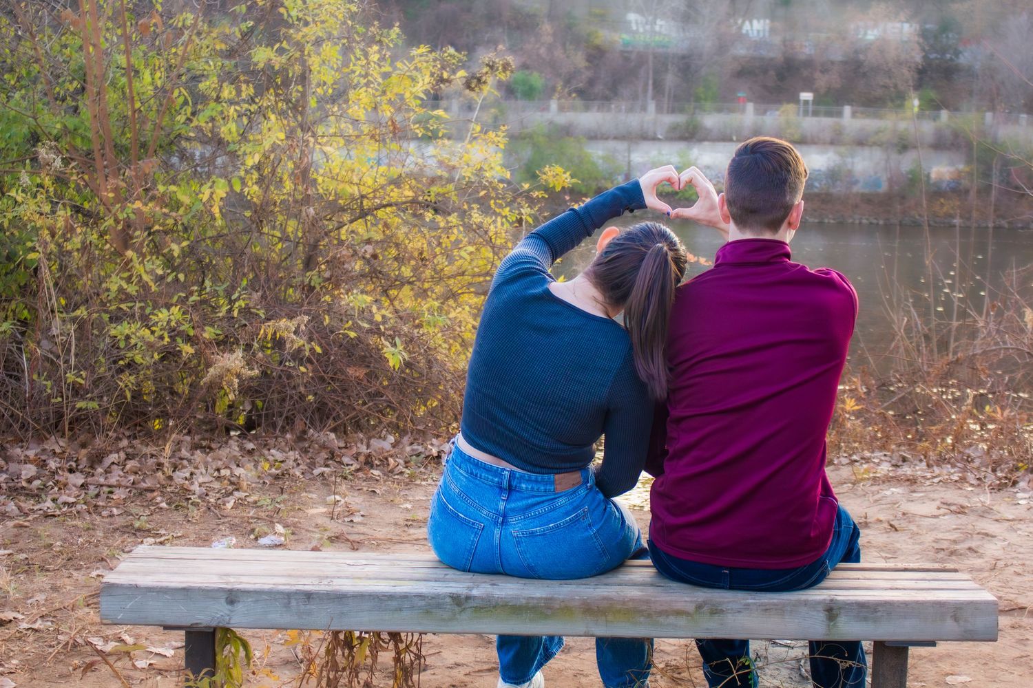 Two people sitting together on a bench overlooking an autumn landscape.