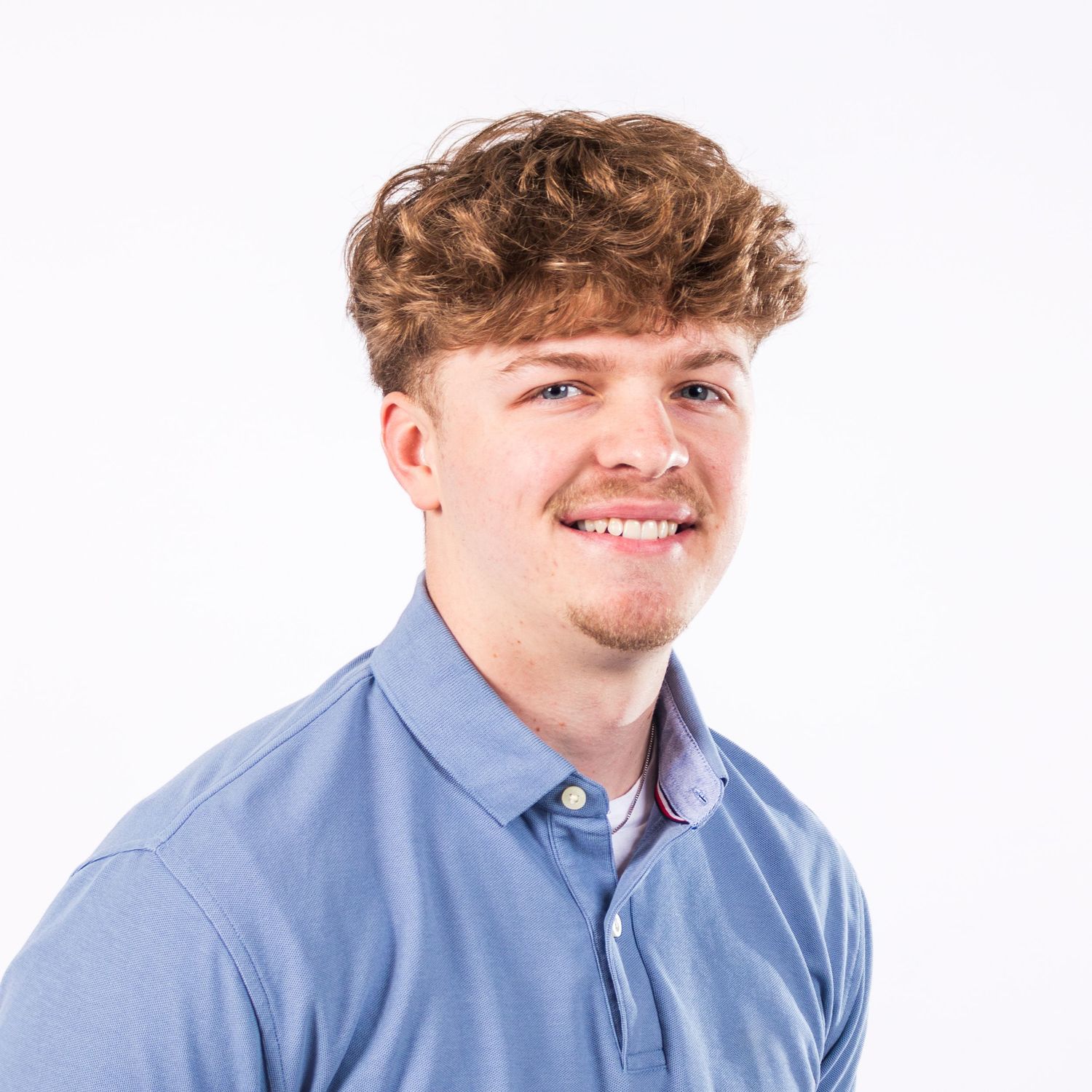 Professional headshot of a person in a light blue collared shirt against a white background, smiling warmly.