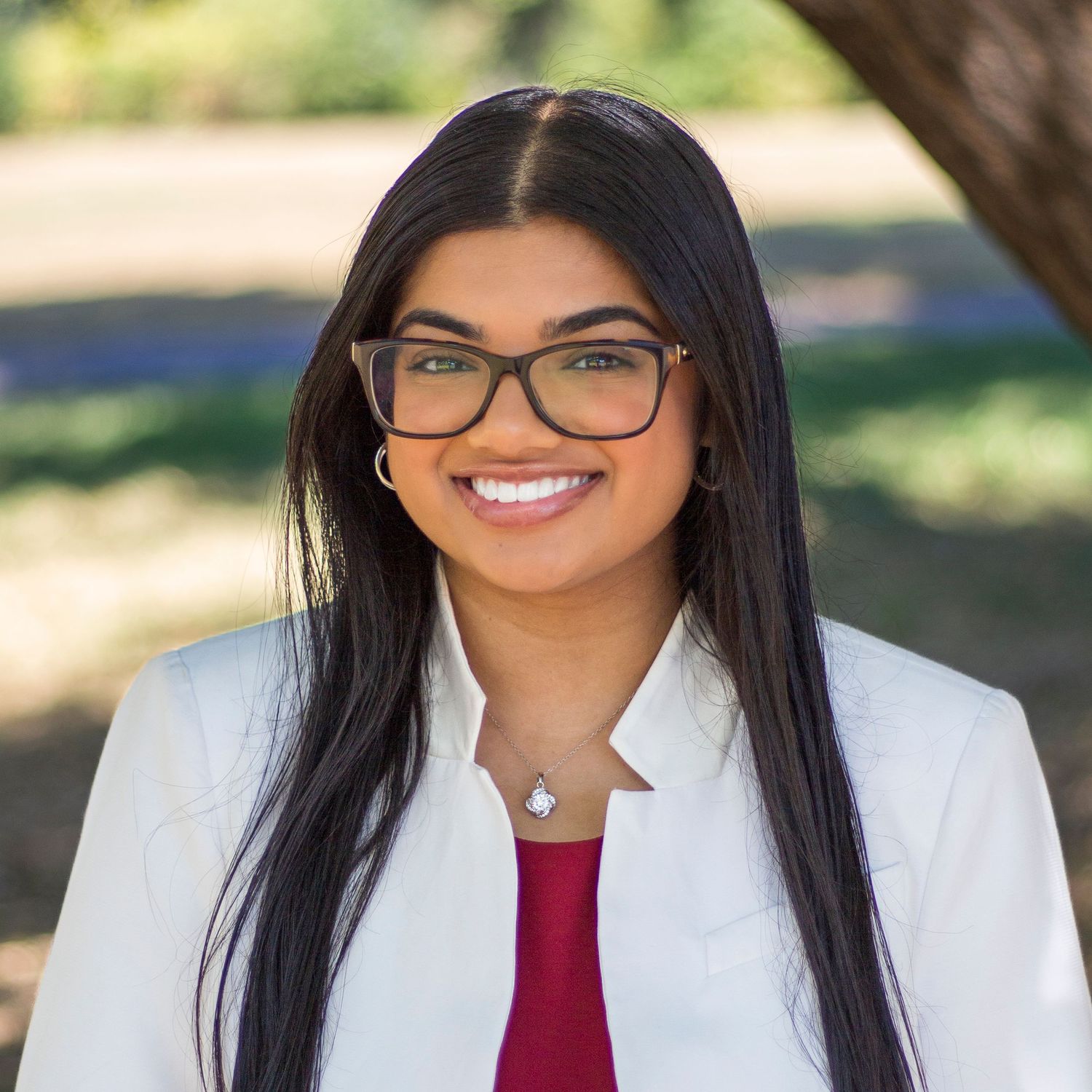 Professional headshot portraits with dark hair and glasses wearing white and burgundy attire in outdoor setting.