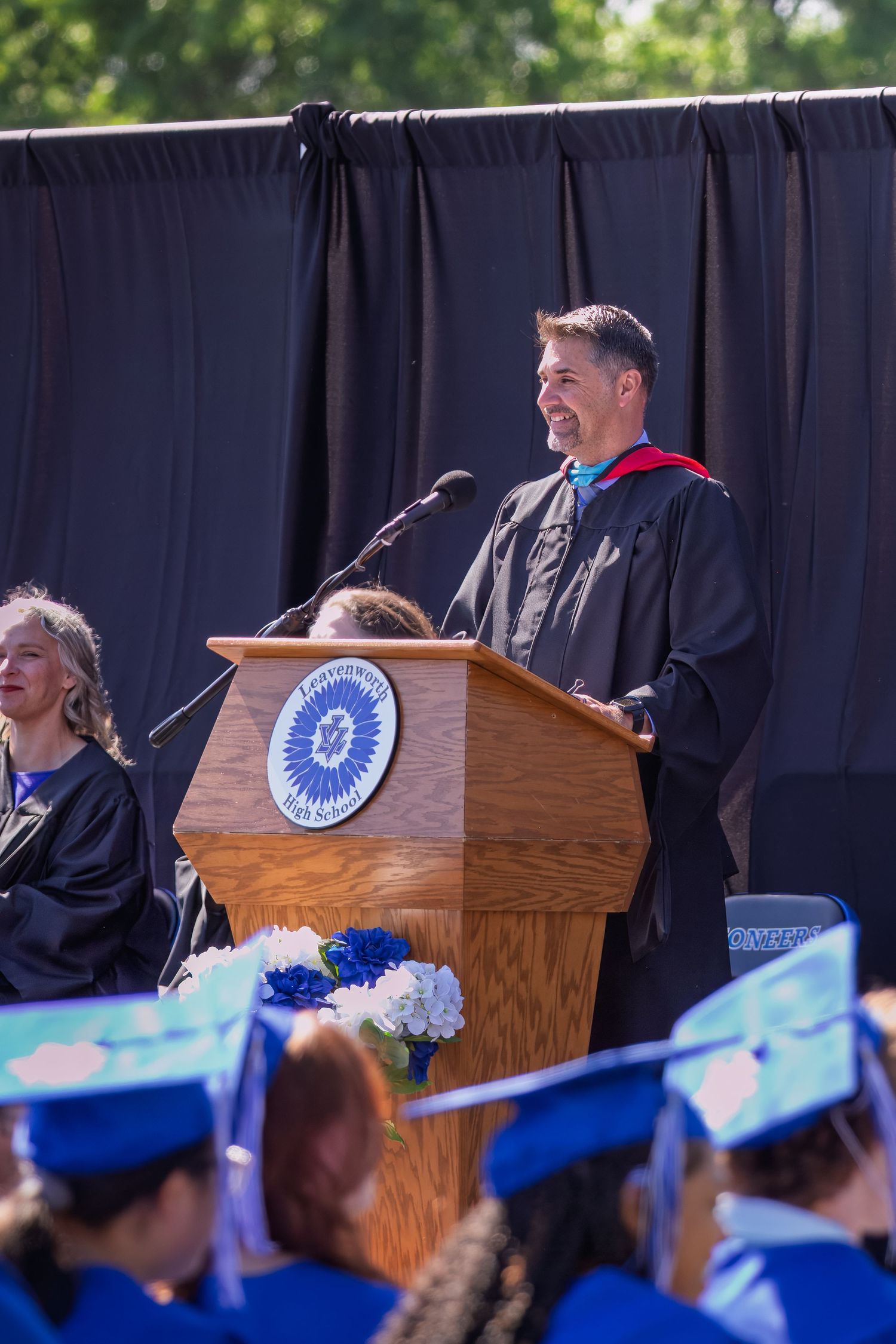 Graduation ceremony podium with wooden lectern and blue diploma covers arranged in front of dark backdrop.