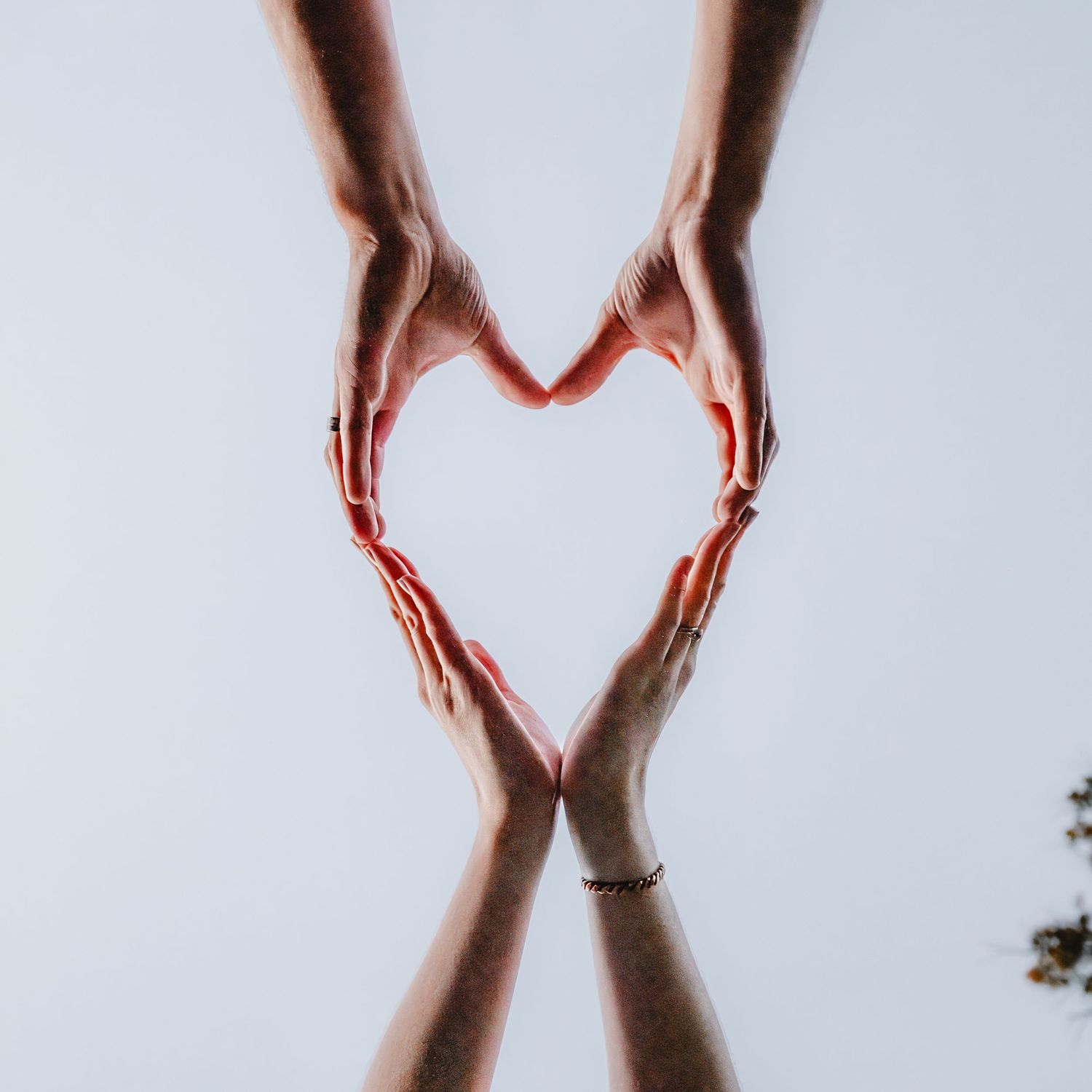 Hands forming a heart shape silhouetted against a bright white background.