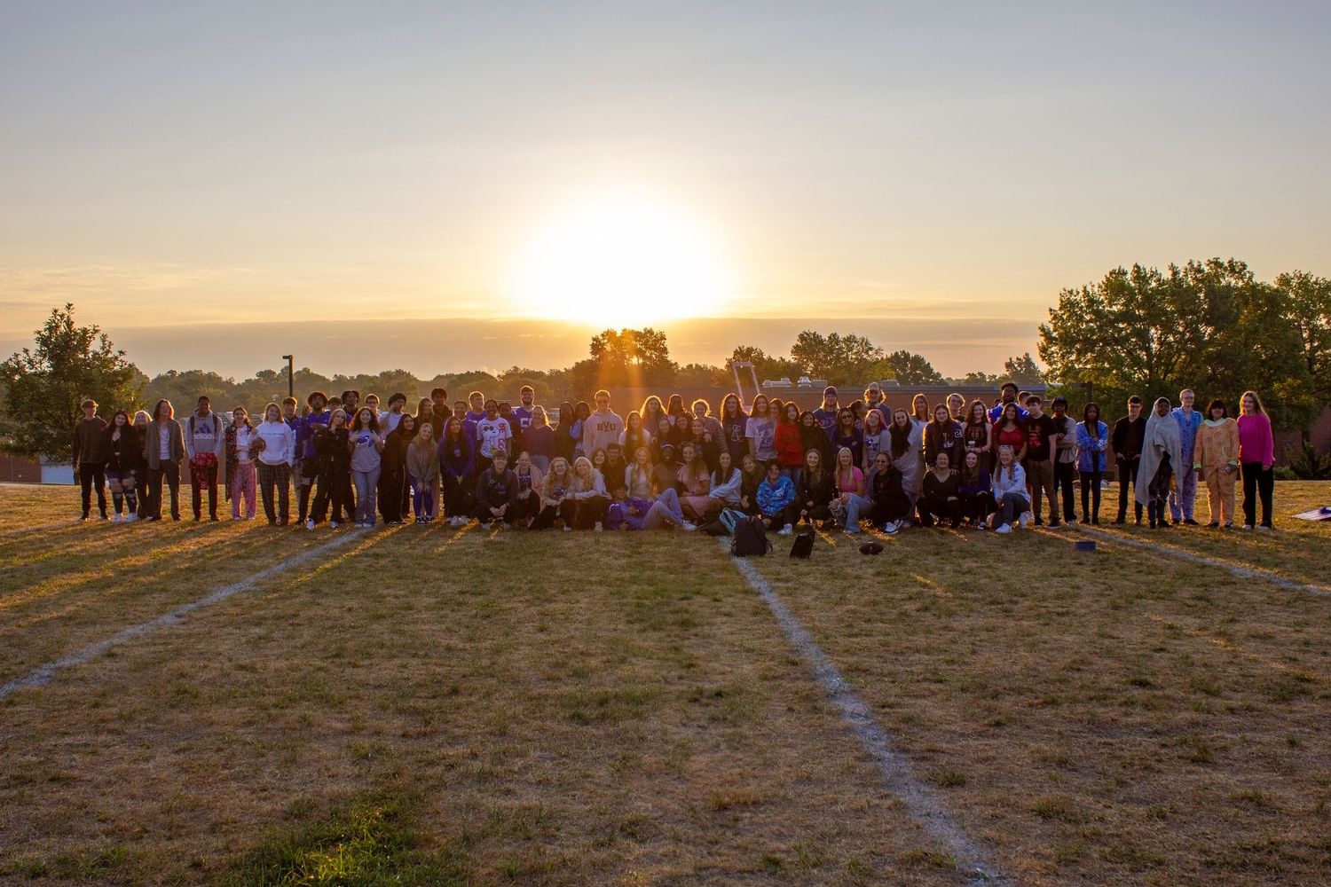 A large group of people gathered outdoors on a hilltop at sunset for a community event or group photo.