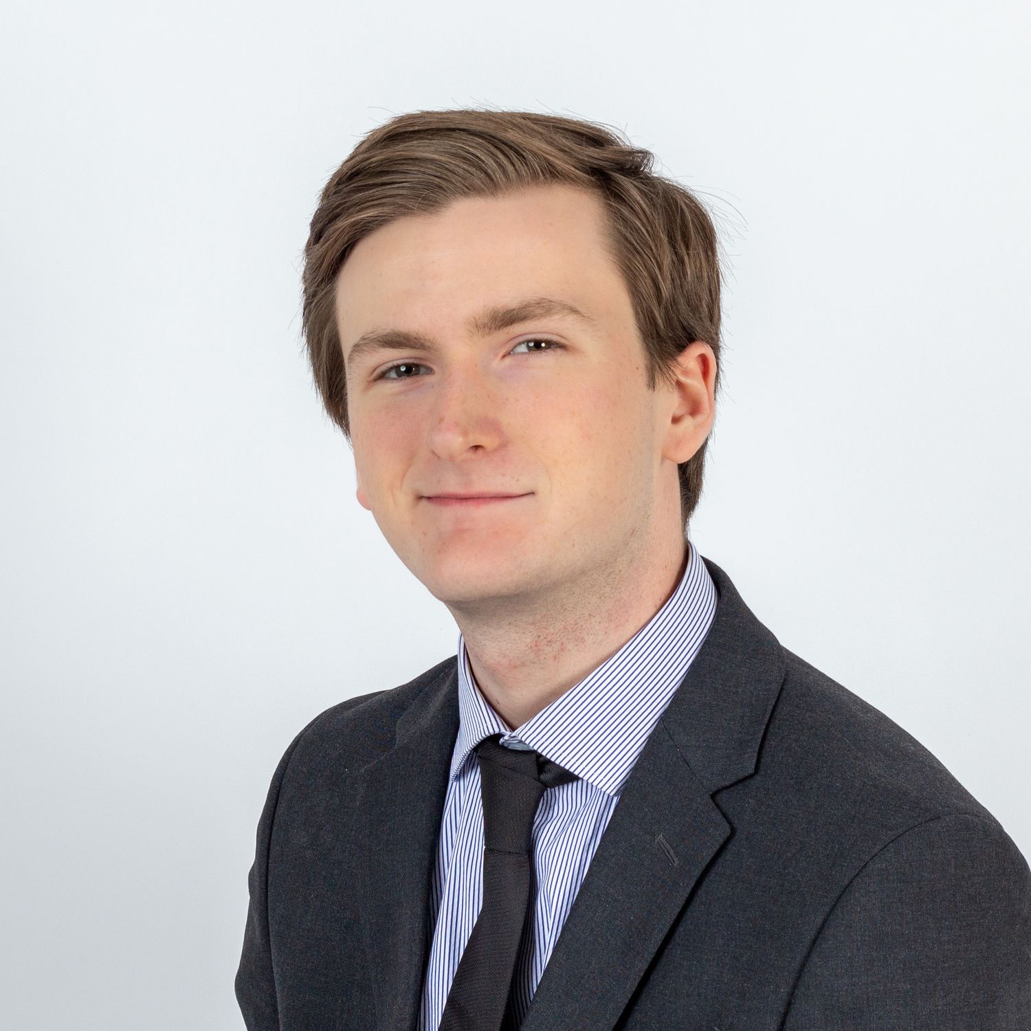 Professional headshot of a person wearing a charcoal suit jacket, light blue dress shirt and navy tie against white background.