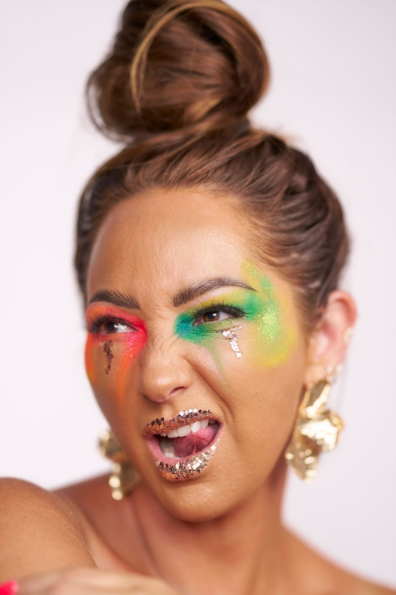 Creative beauty portrait with colorful neon eyeshadow, glitter lips, and upswept hair against white background.