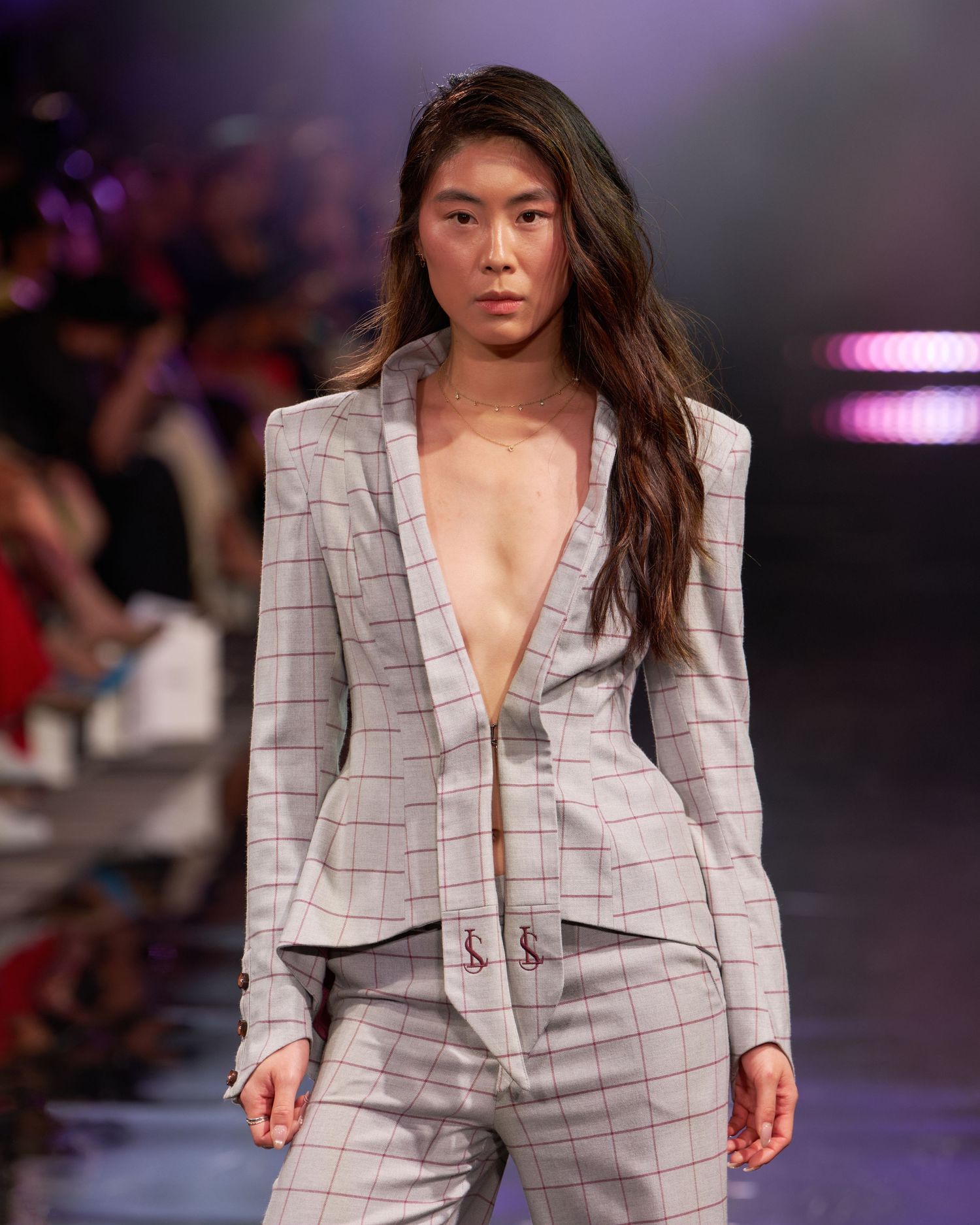 Model walks runway in a plunging grey plaid blazer suit at a fashion show.