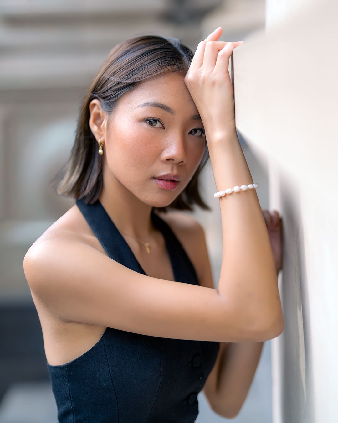 Fashion portrait of model in elegant black sleeveless top posing against light background with pearl bracelet.