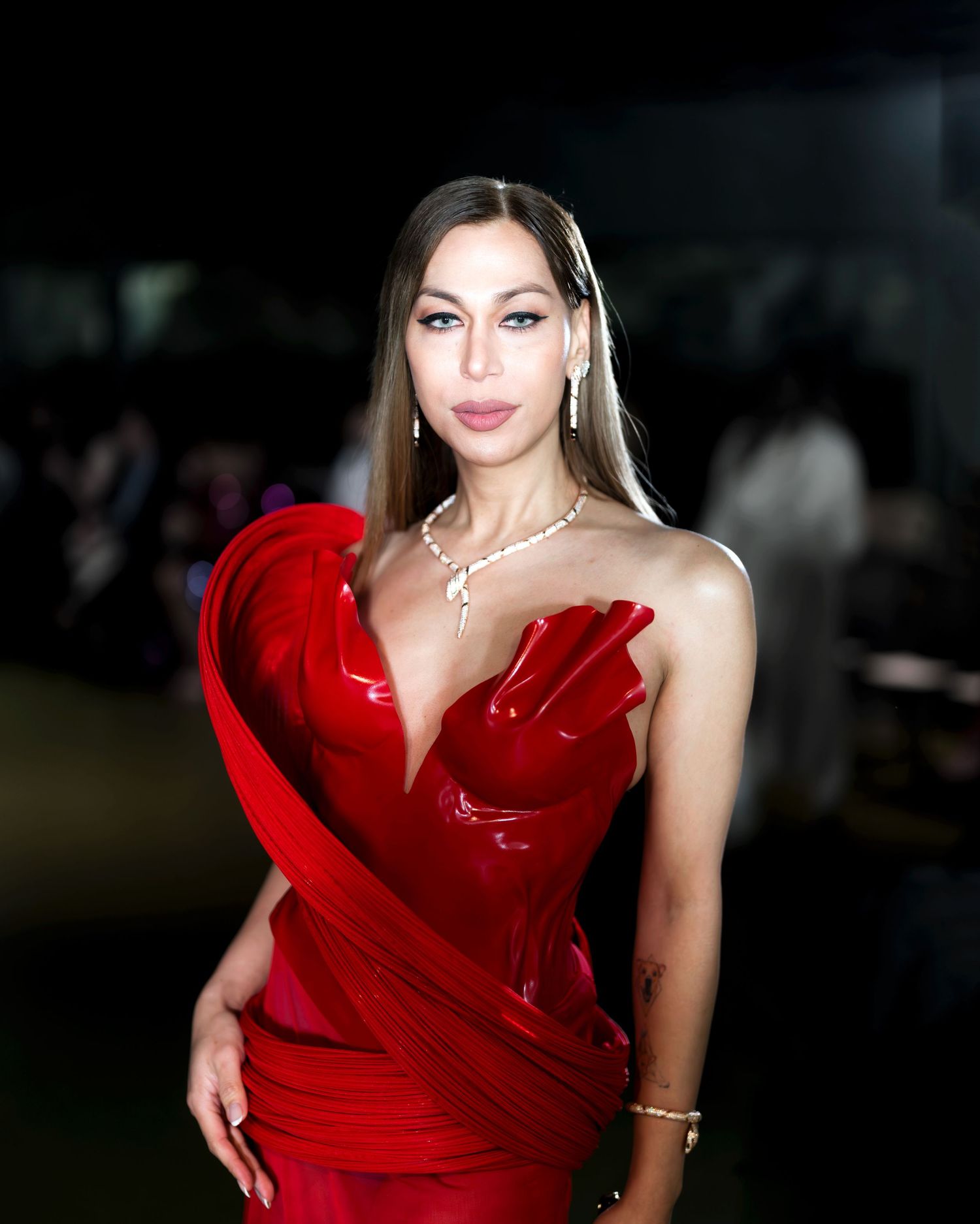 A glamorous model in a striking red evening gown poses elegantly against a dark background.