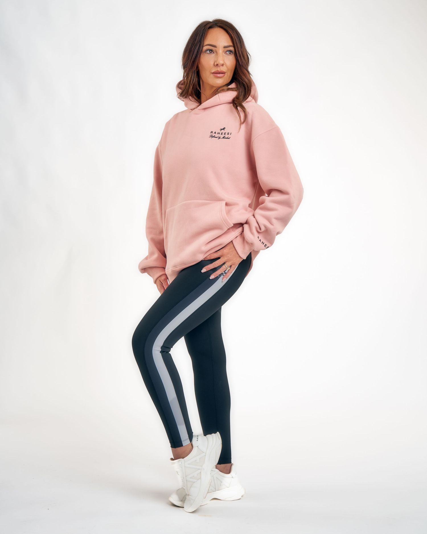 Woman wearing oversized pink hoodie and dark navy striped leggings with white sneakers on white background.