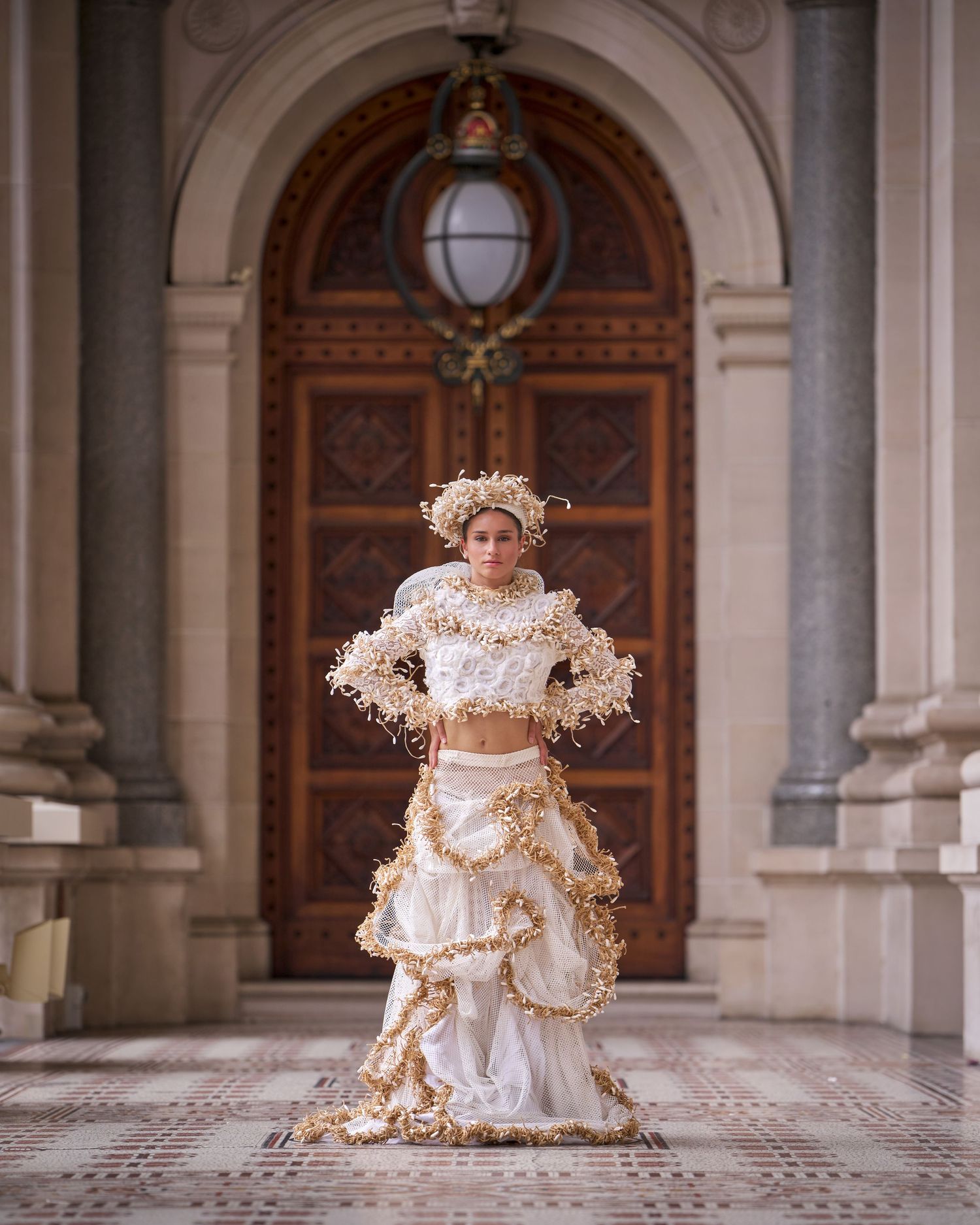Elegant figure in a white Victorian-style dress poses gracefully in a grand arched hallway with ornate architecture.
