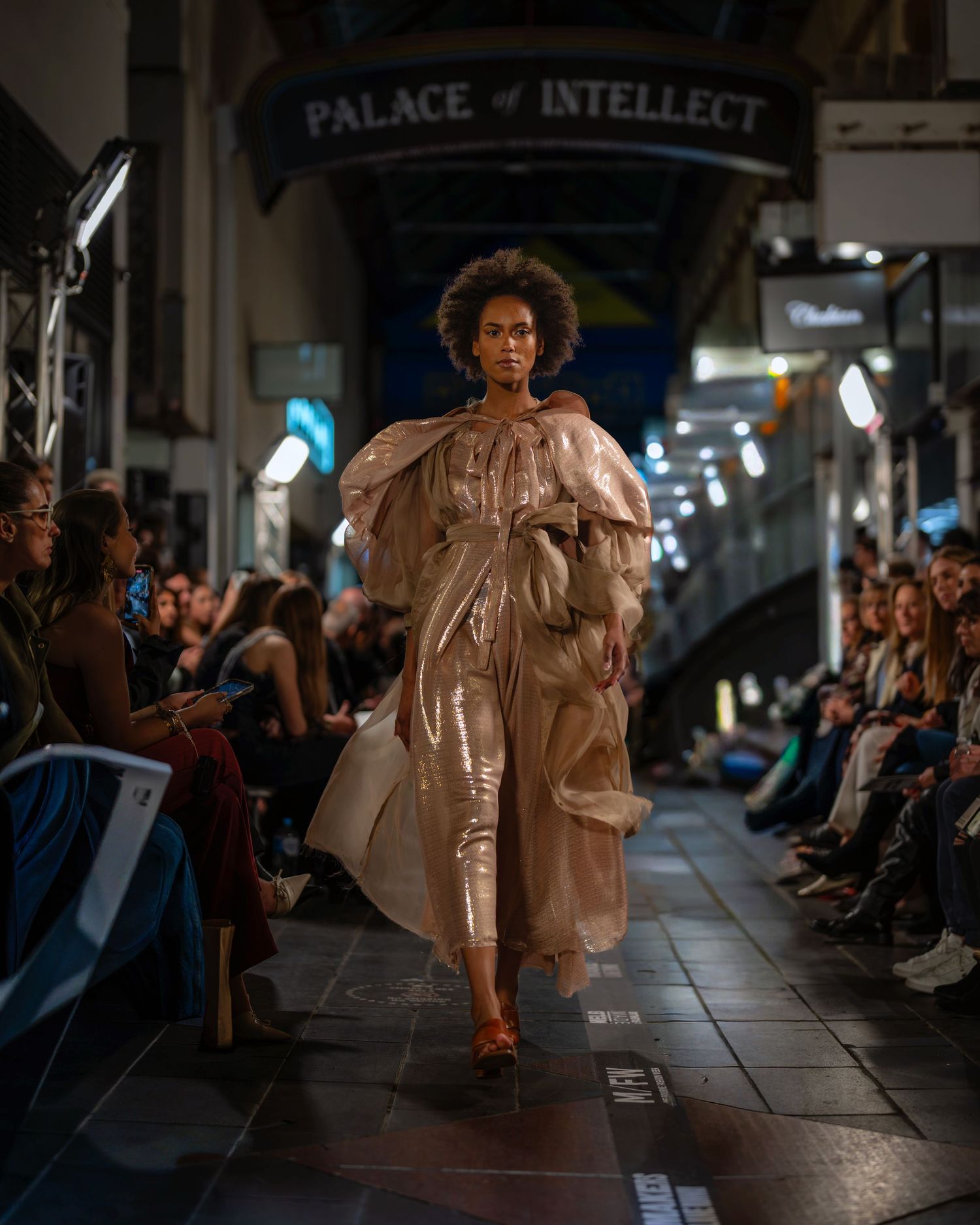 A model walks the runway in a flowing metallic bronze dress during a fashion show at the Palace of Intellect.