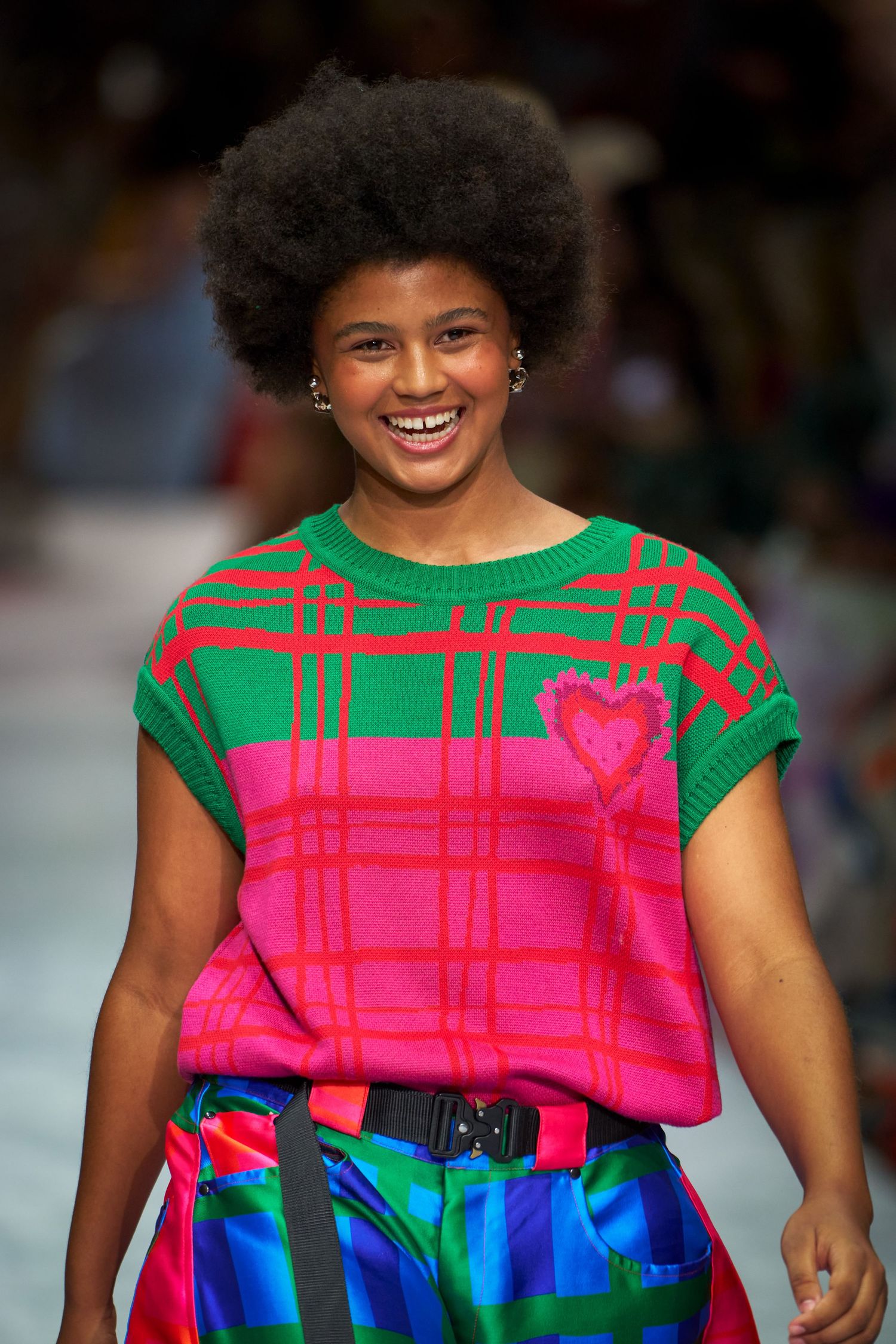 Model walks runway in vibrant color-block dress featuring bright pink top and electric blue skirt with black belt.