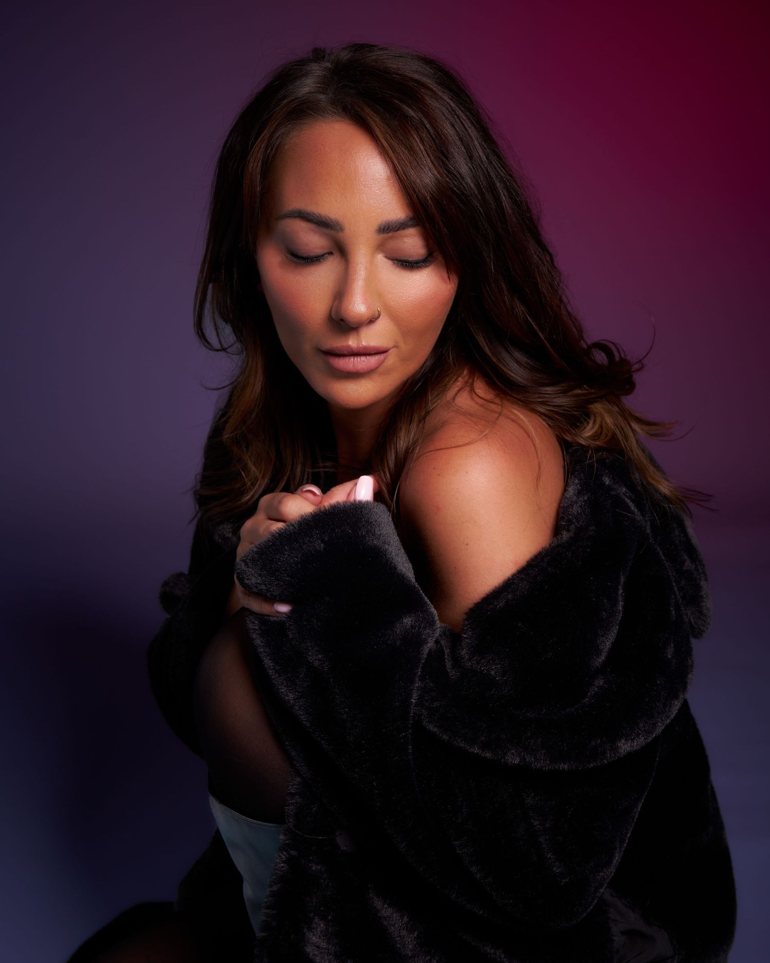 Woman in black fur coat poses elegantly against purple backdrop with eyes closed.