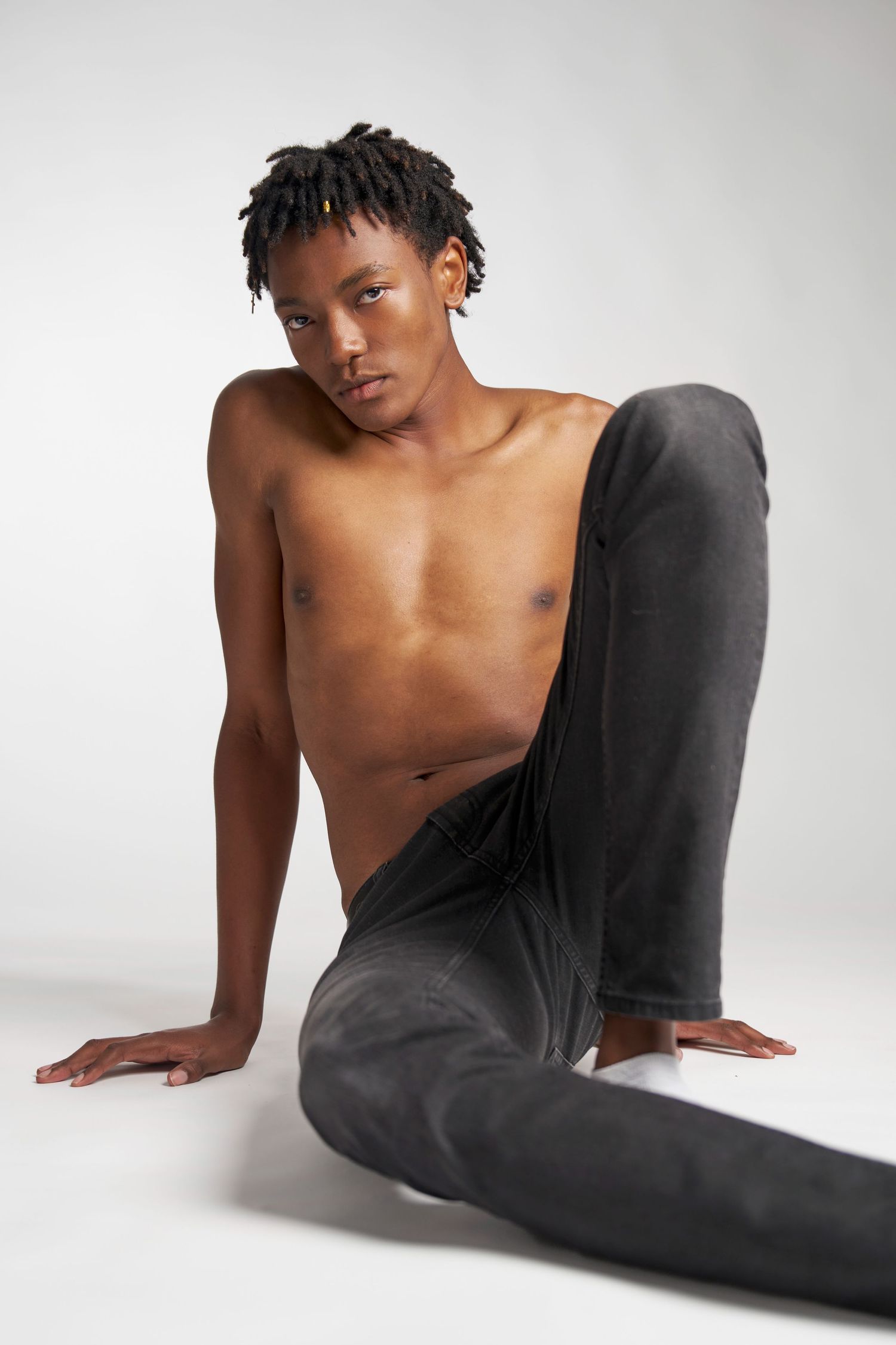 Artistic portrait of a shirtless model wearing black pants posing on a white studio background.