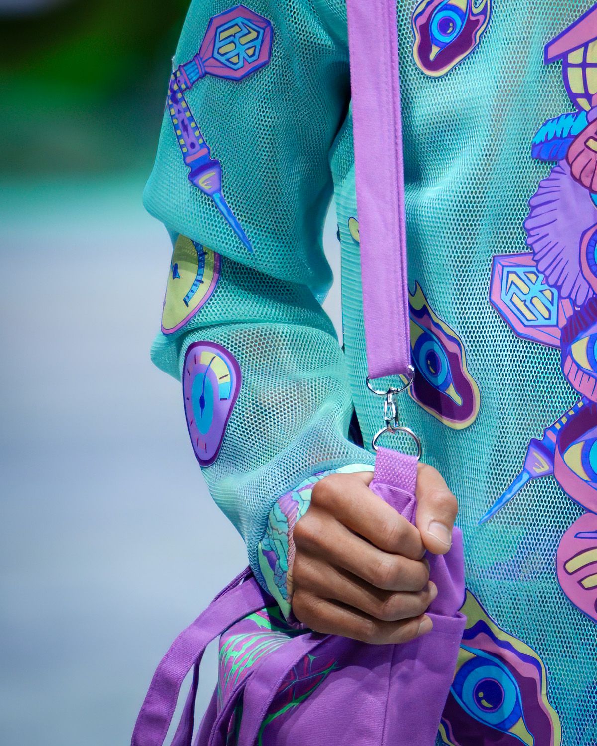 Close-up of a teal backpack with colorful crystal and gem pattern designs and purple straps.