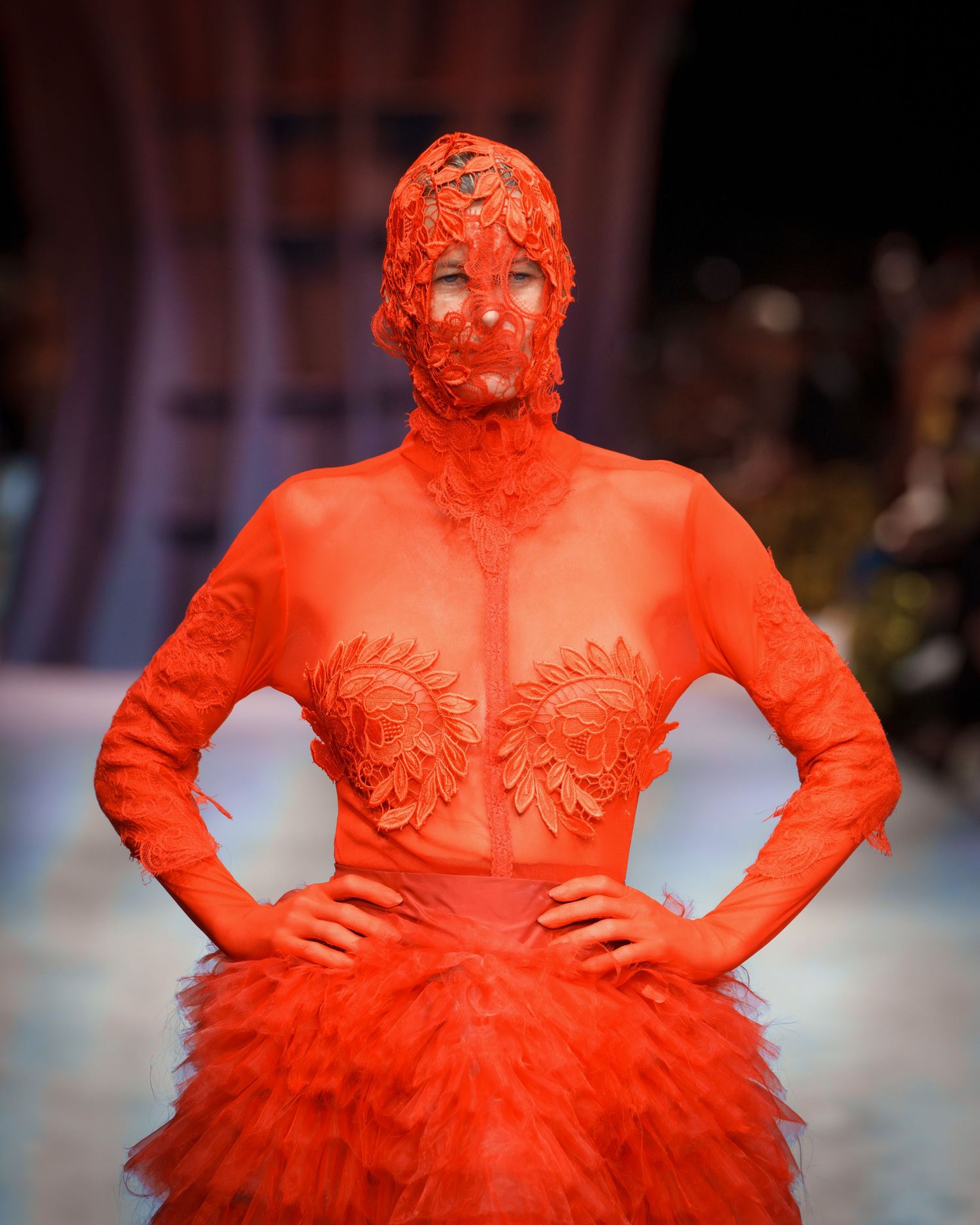 Model wearing a striking all-red ensemble featuring a sheer bodice and dramatic tulle skirt on the fashion runway.