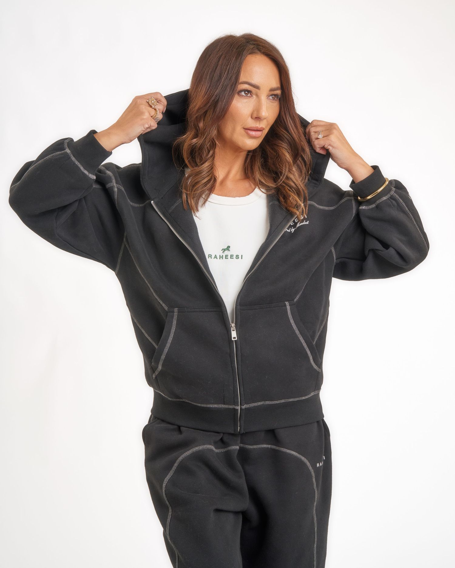 Woman wearing a black zip-up hoodie with contrast stitching and matching joggers from Raheesi.