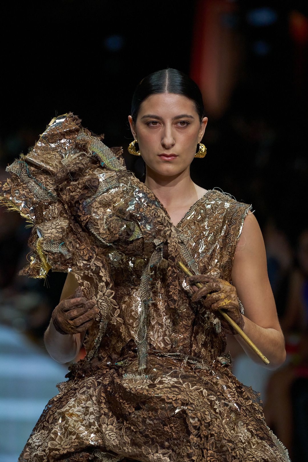 Model walks runway in avant-garde gold metallic sculptural dress with dramatic ruffled details at fashion show.