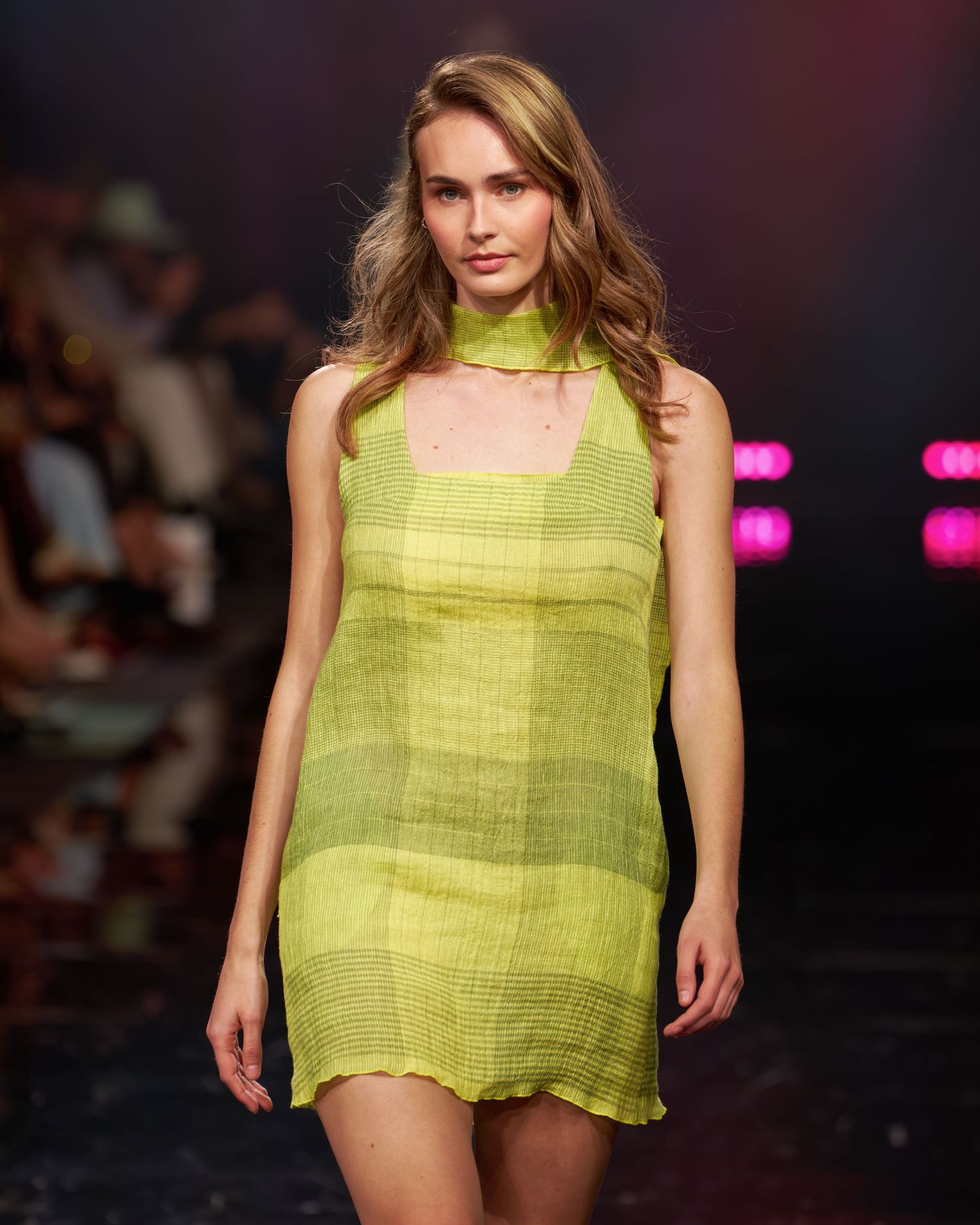 Model walks runway in a lime green sheer mini dress with halter neck at a fashion show.