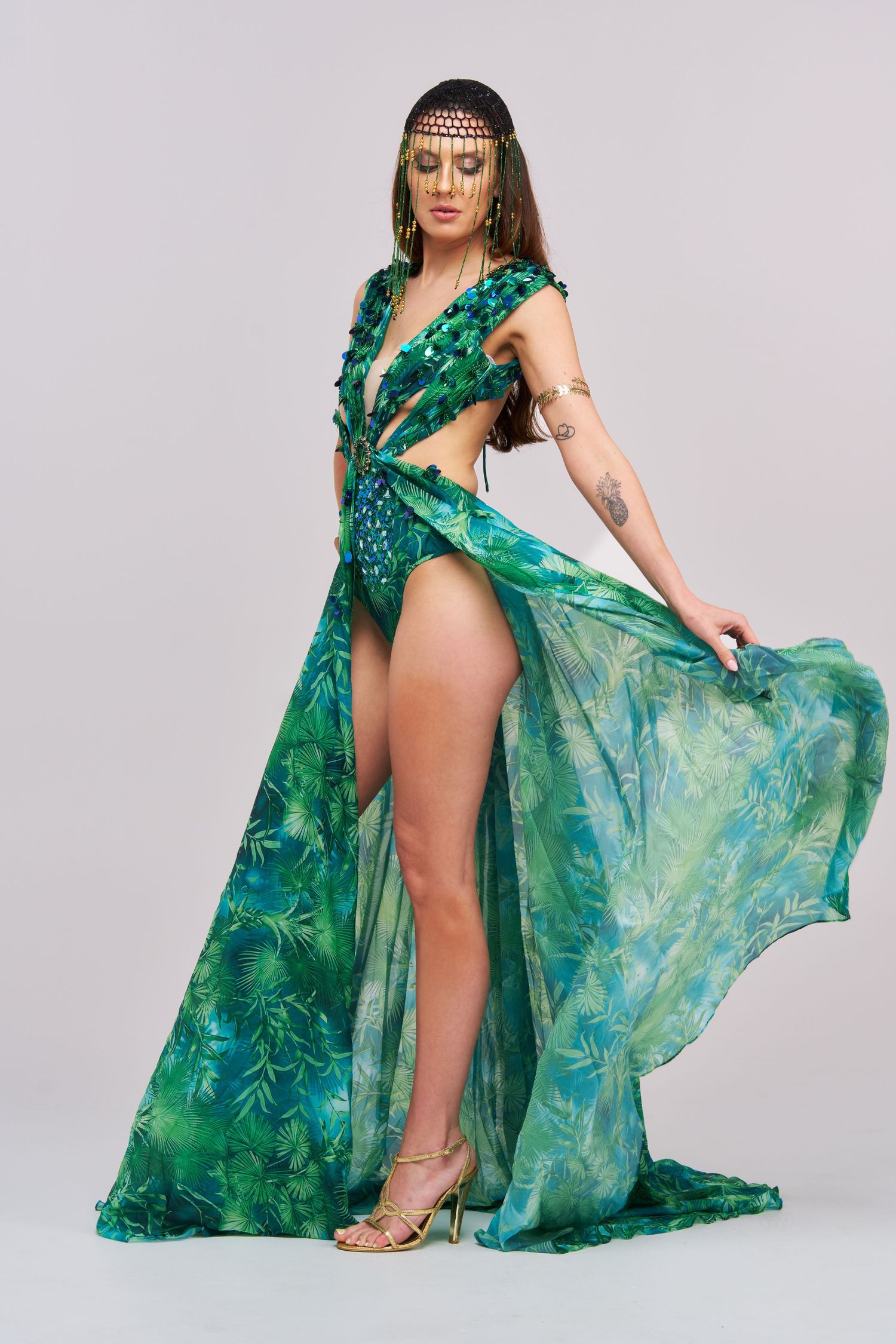 A model poses in a flowing emerald green silk dress with watercolor patterns against a light studio background.