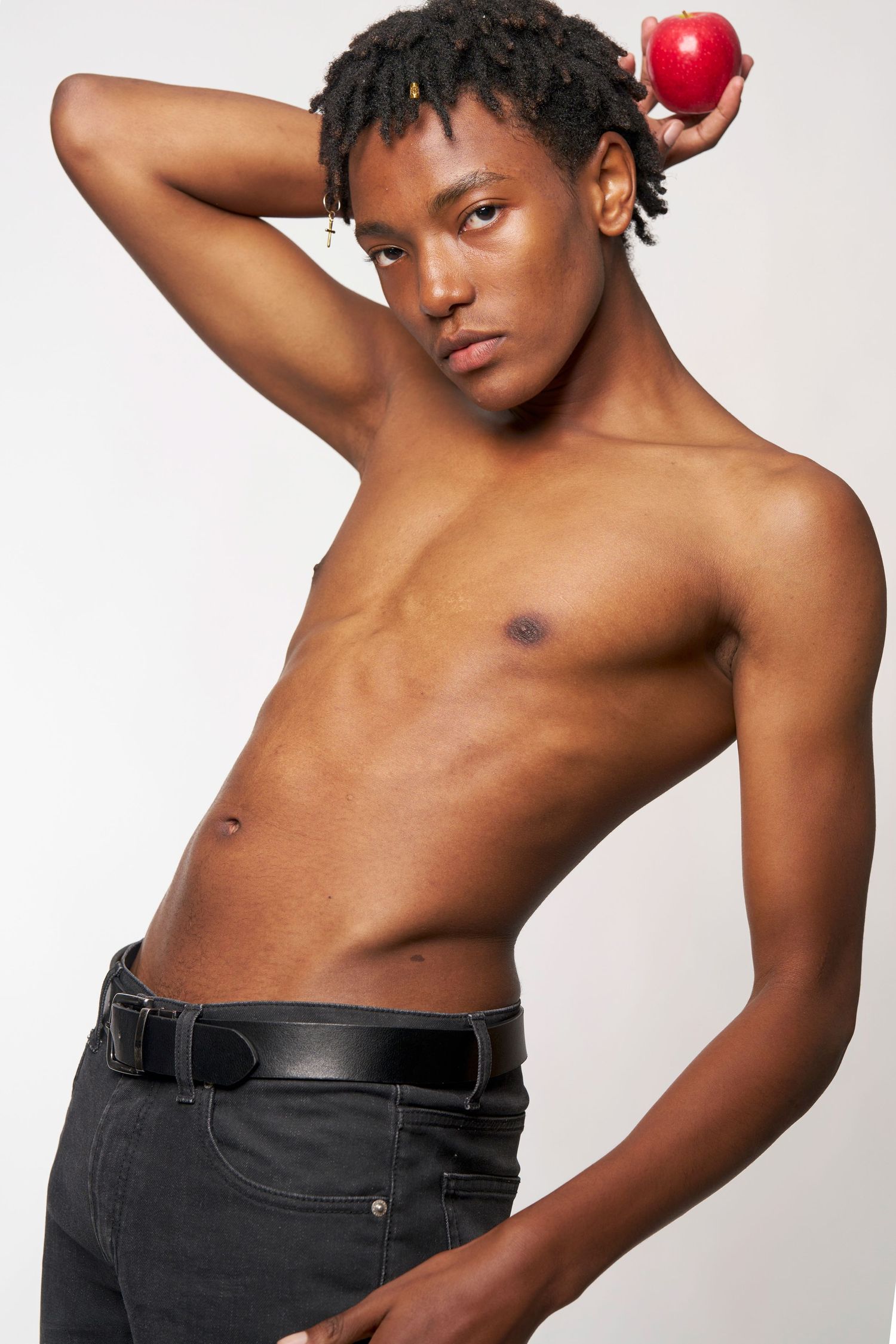 Shirtless person in black jeans poses against white background while holding red apple in artistic photo sequence.